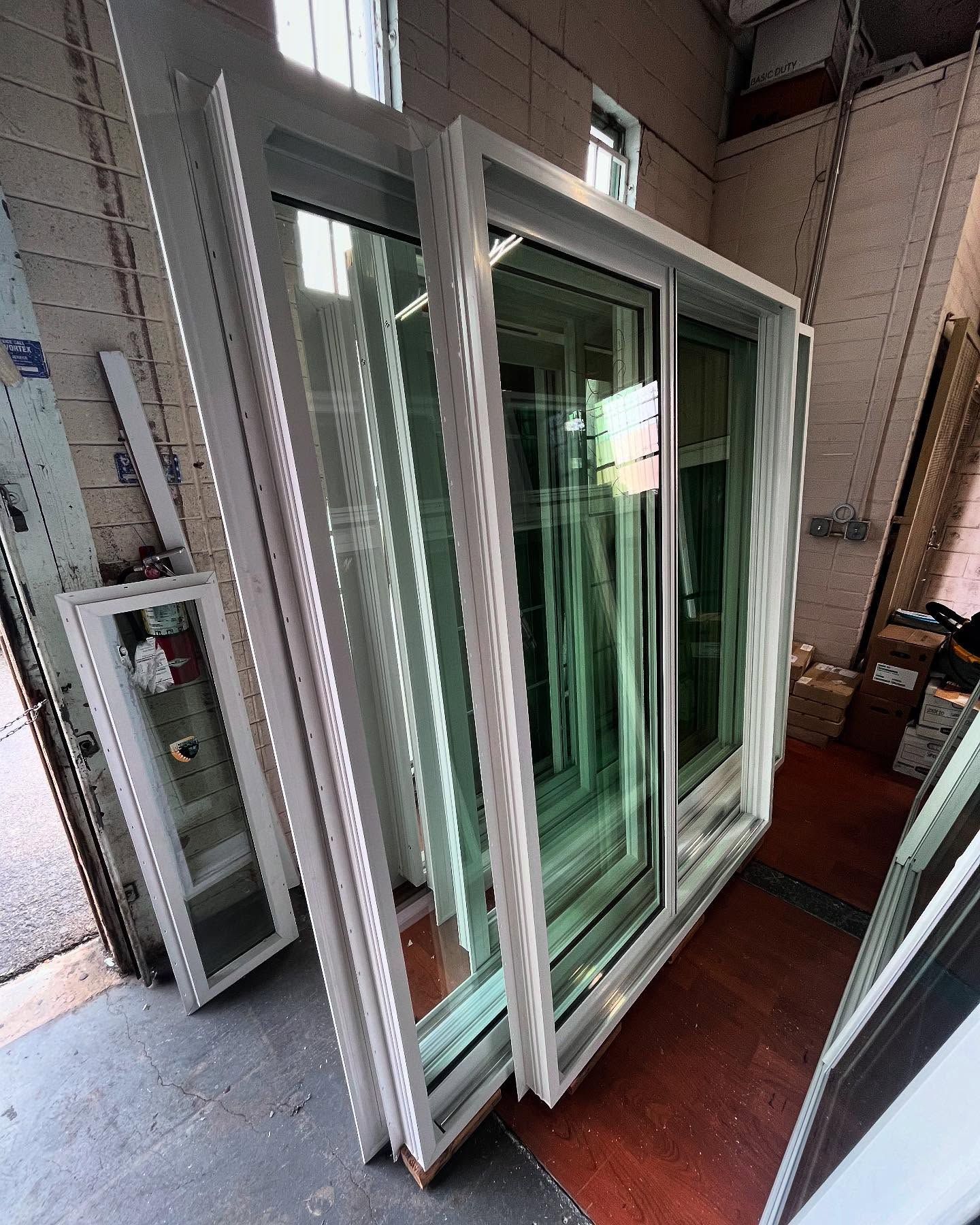 Stacked white sliding glass doors leaning in a workshop or storage area.