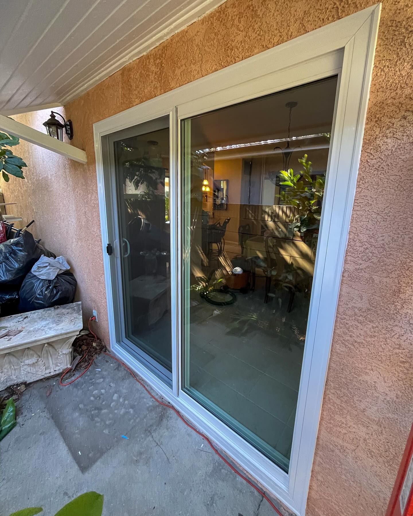 Sliding glass patio door with white frame and peach stucco wall beside a bench and outdoor seating area