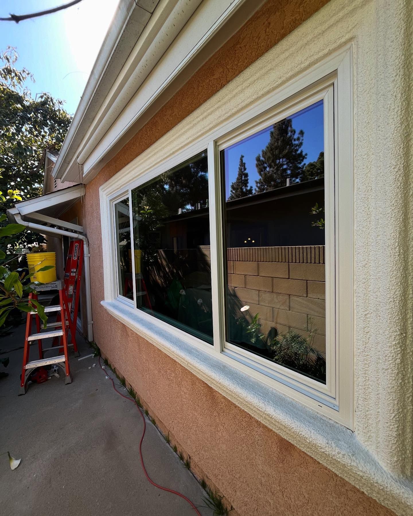 House exterior with new white-framed windows beside a ladder on a narrow walkway