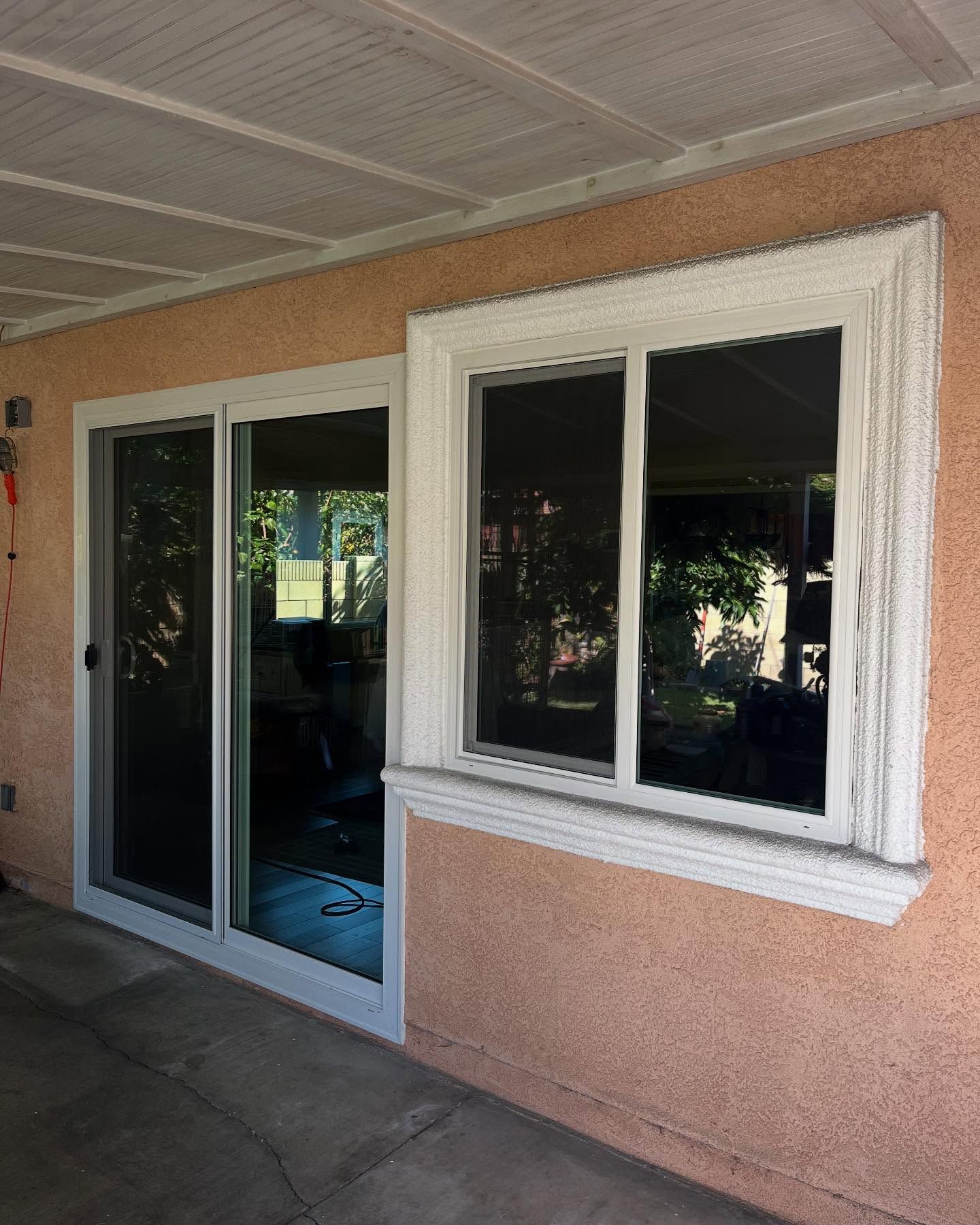 Sliding glass door and white-framed windows on a stucco exterior wall under a covered patio.