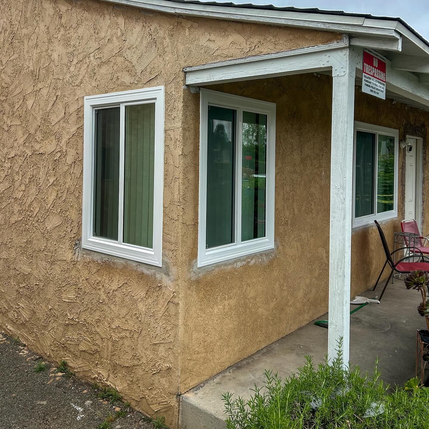 Stucco house corner with white-trimmed windows and small front porch