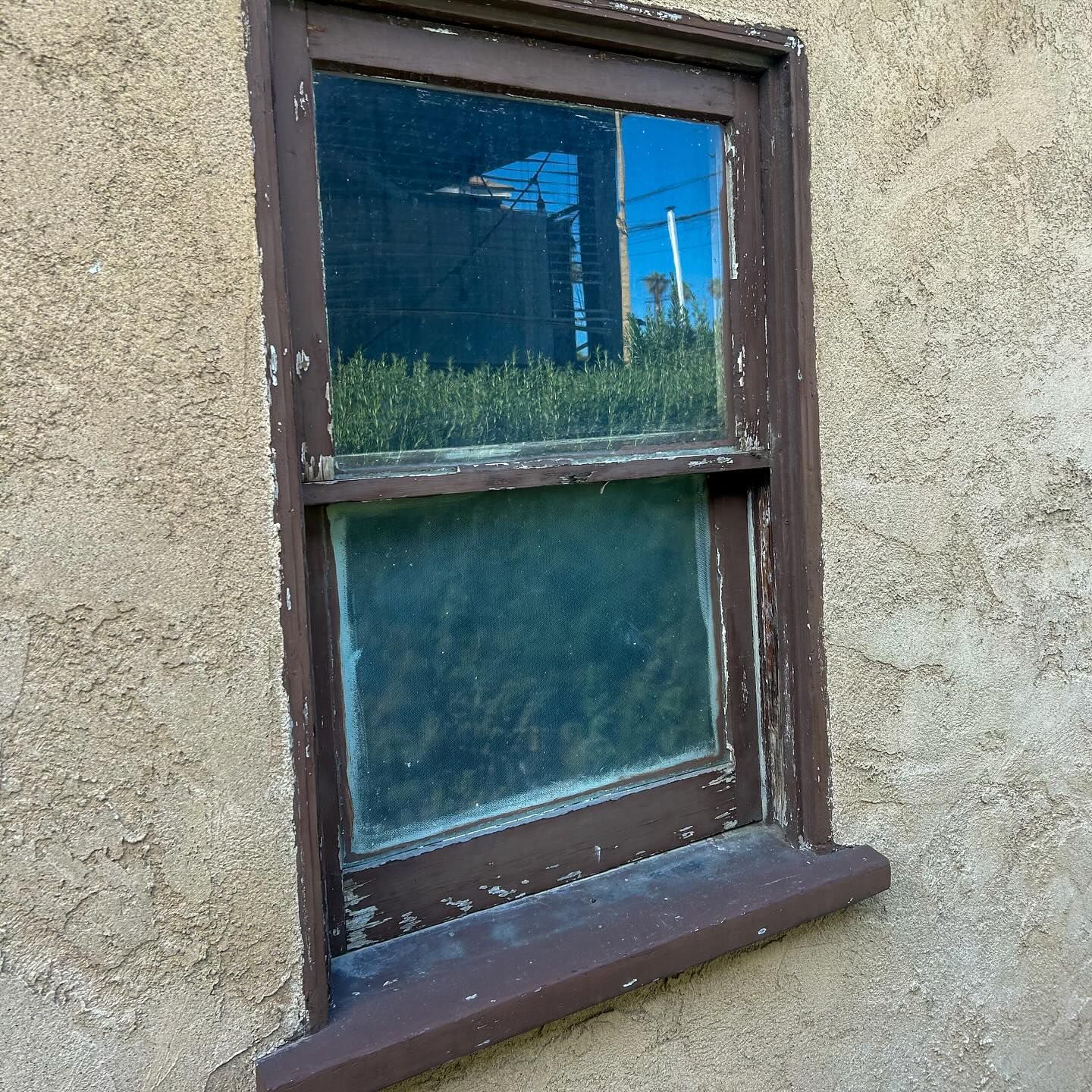 Old brown-framed window set in a rough beige stucco wall, with reflective blue glass.