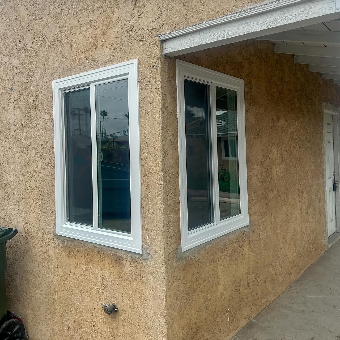 Tan stucco house exterior with white-trimmed windows and a covered entryway