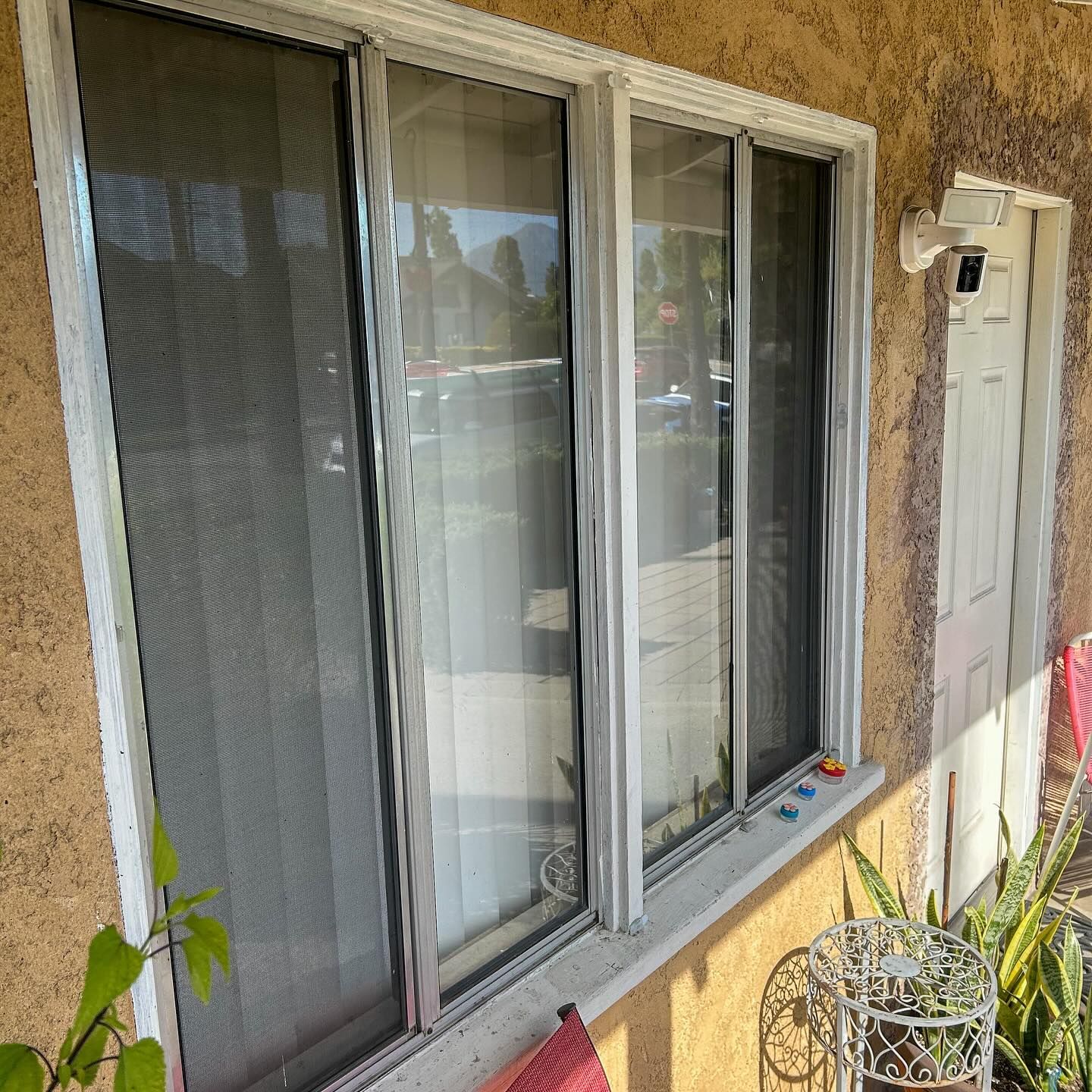 Stucco house exterior with white-framed windows, a front door, and a small metal table on the porch