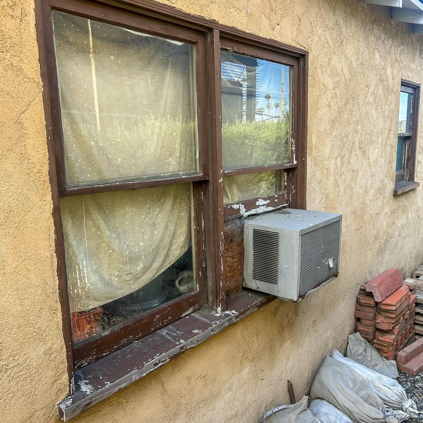 Exterior wall with two brown-framed windows and a window air conditioner installed beneath one window.