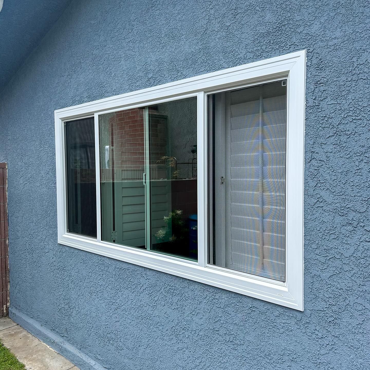 White-framed sliding window in a blue stucco exterior wall