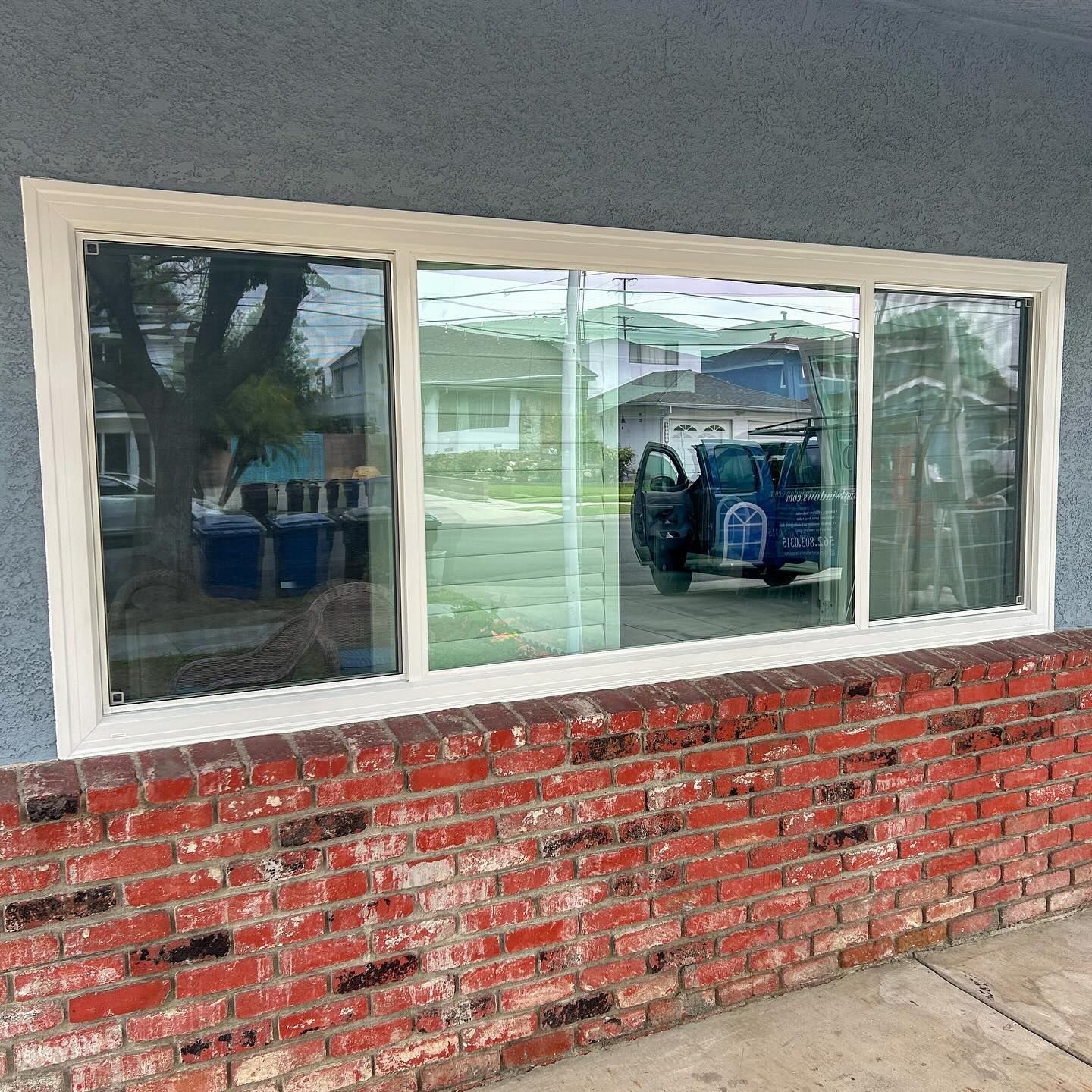 Storefront window with white trim above a red brick wall, reflecting the street and a parked vehicle.