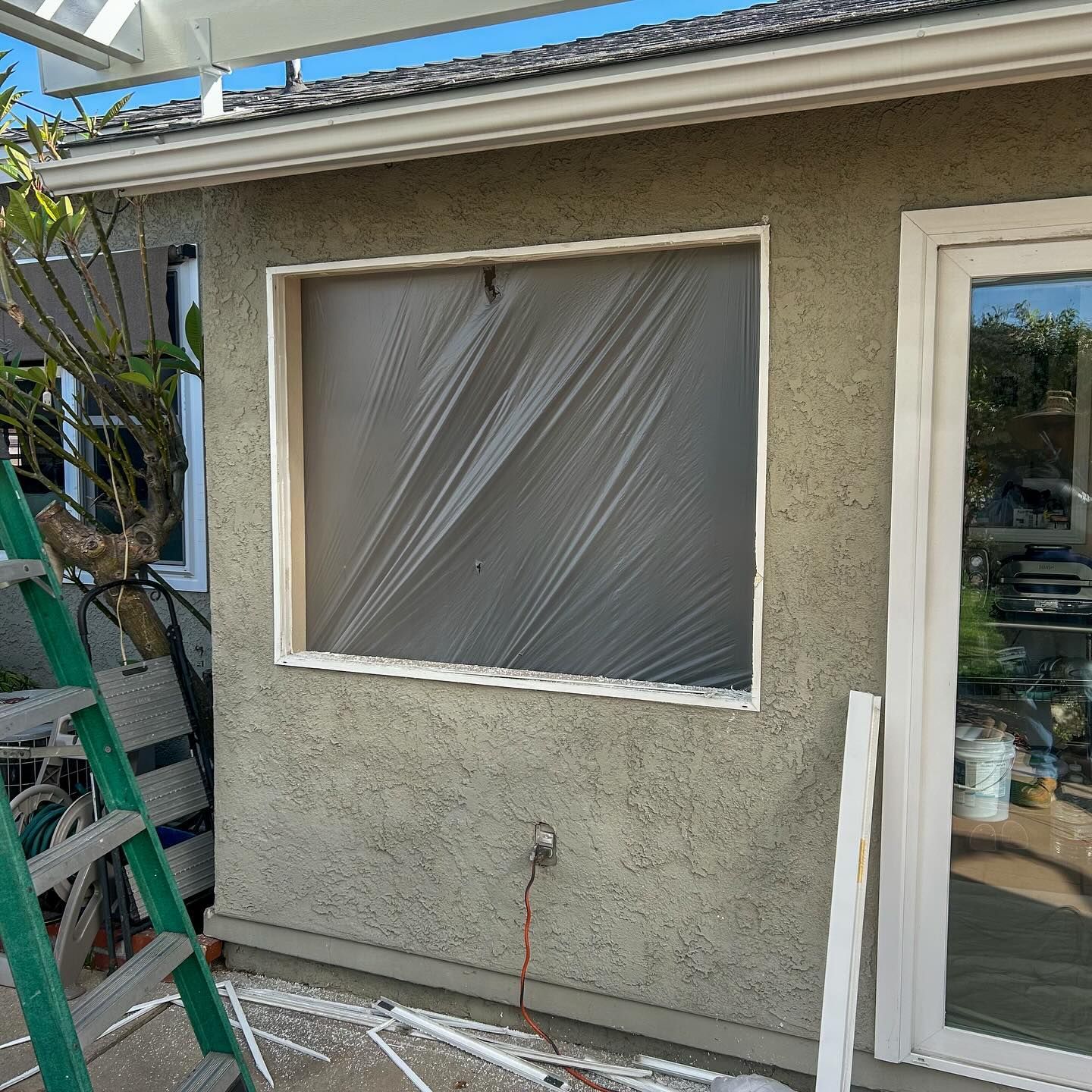 Exterior stucco wall with covered window, glass door, and a ladder leaning beside it.