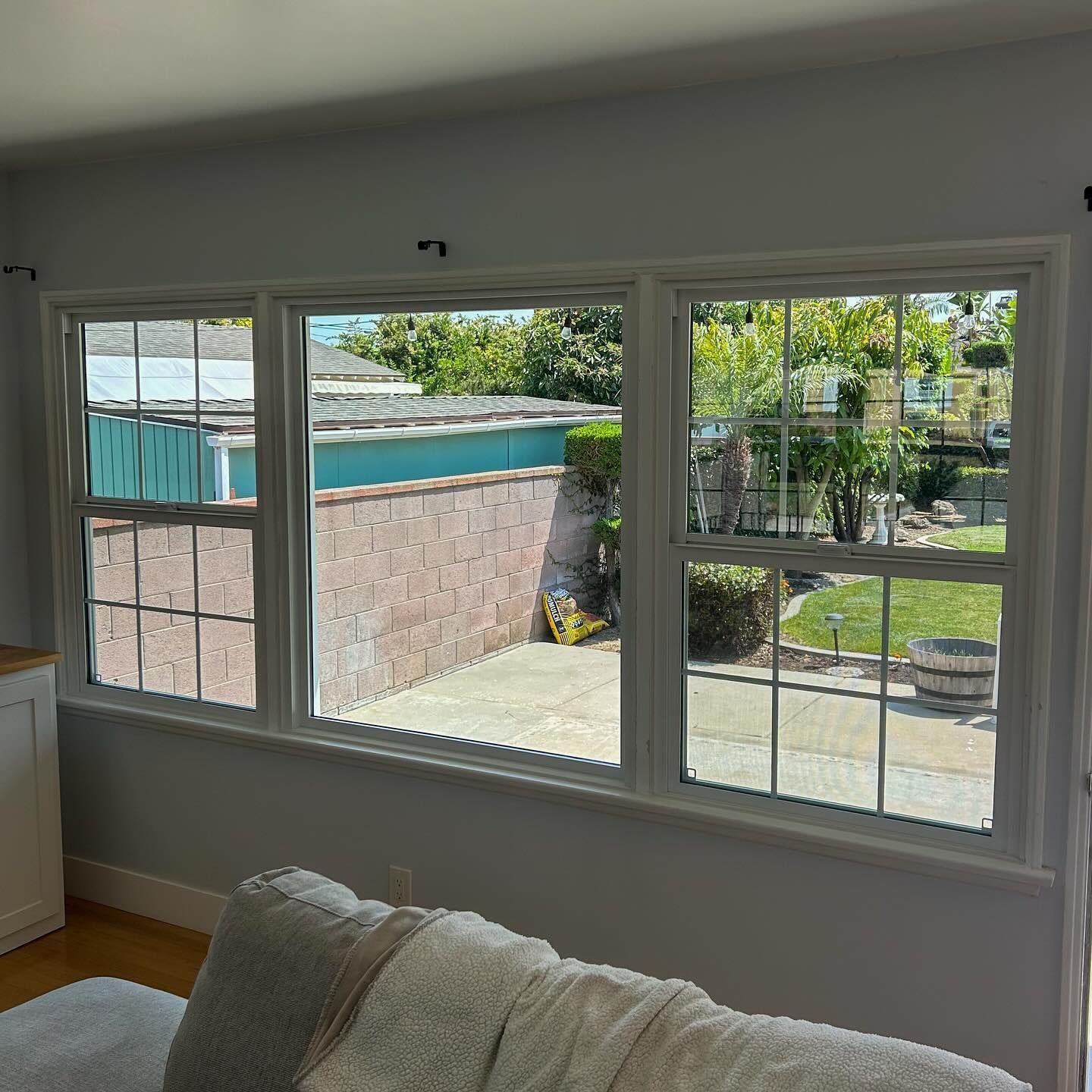 Bright living room window overlooking a patio, brick wall, and backyard greenery