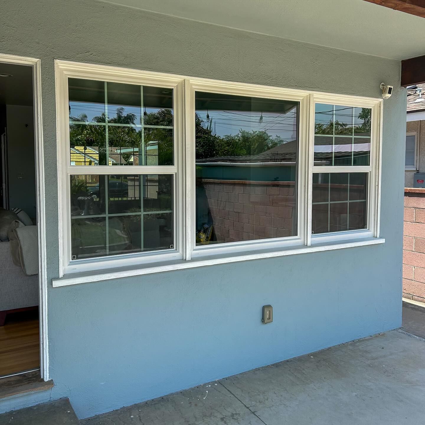 Blue exterior wall with three white-trim windows and a small electrical outlet under a covered patio