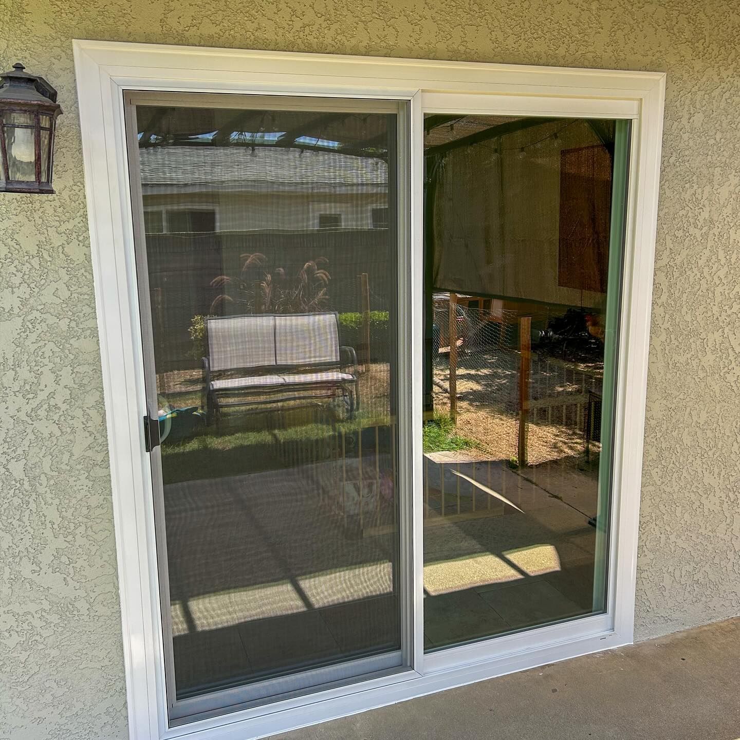 White-framed sliding glass patio door with dark screen, reflecting an outdoor patio and yard