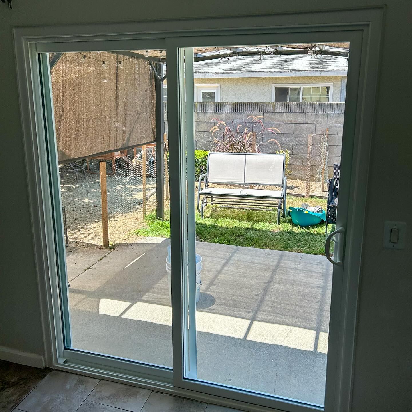 Sliding glass door opening to a sunny patio with a bench and potted plant in a backyard.