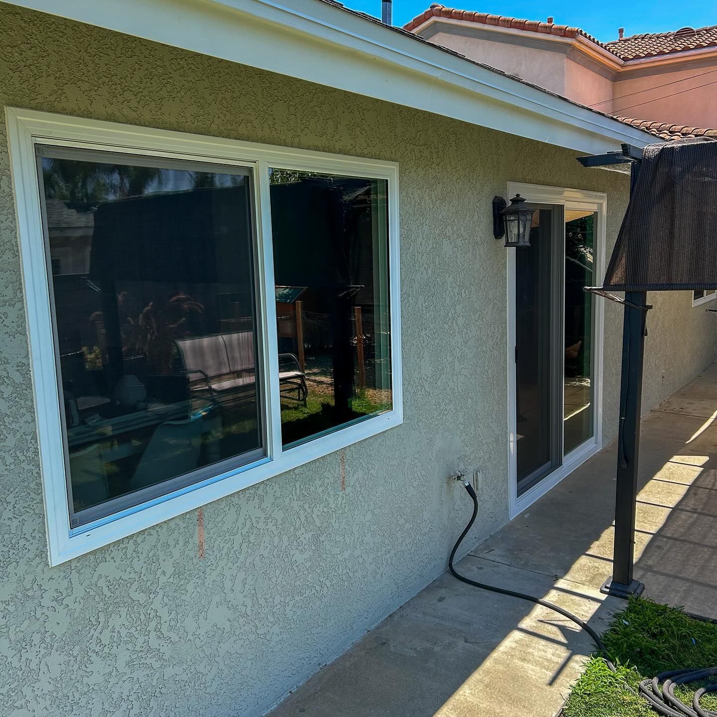 Exterior of a stucco house with a window, glass door, patio, and garden hose on the wall