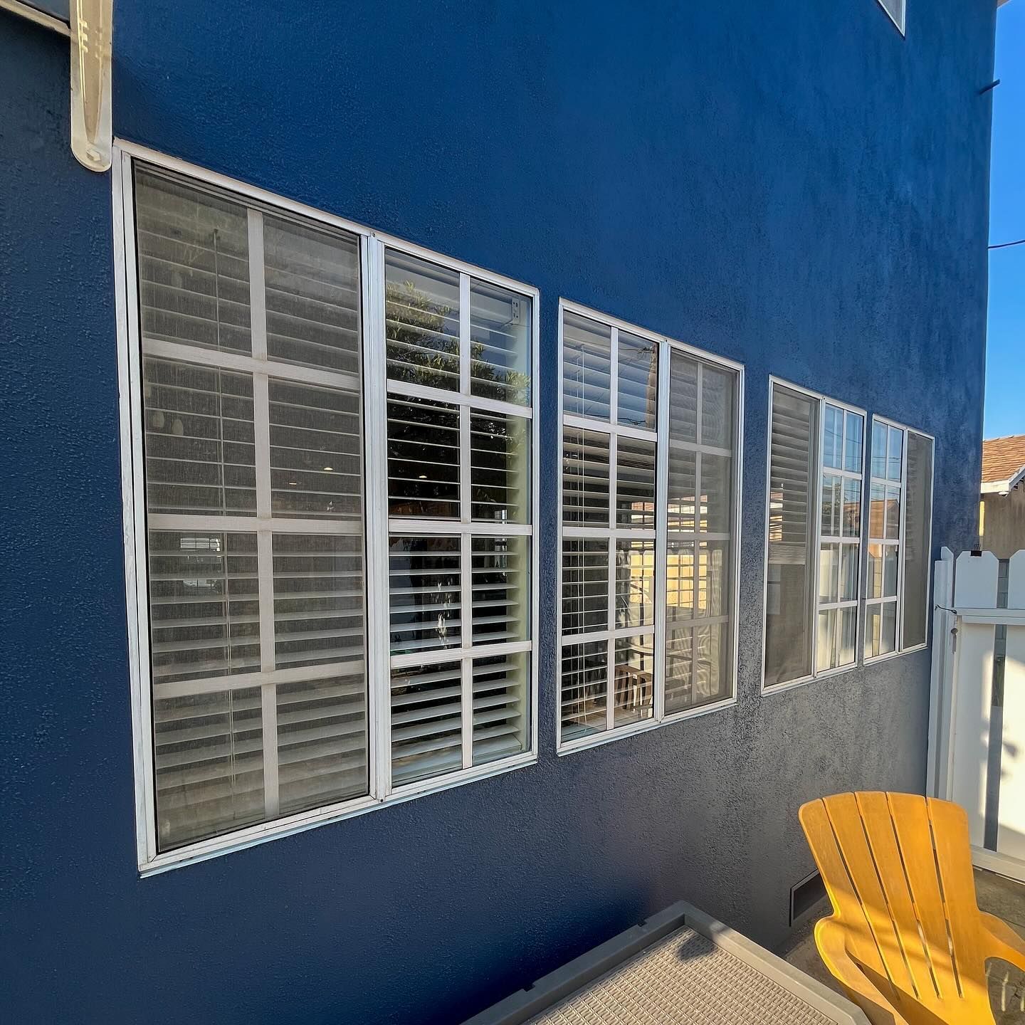 Blue building wall with white louvered windows and a yellow chair on a walkway