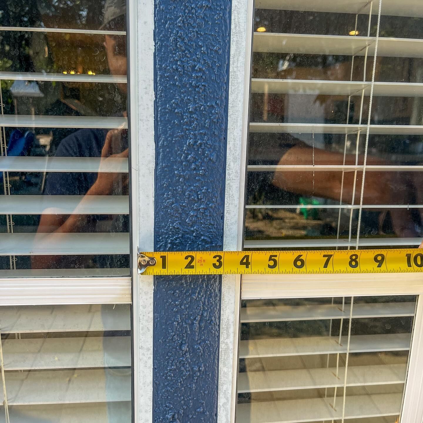 Yellow tape measure stretched across a blue-framed window with white blinds