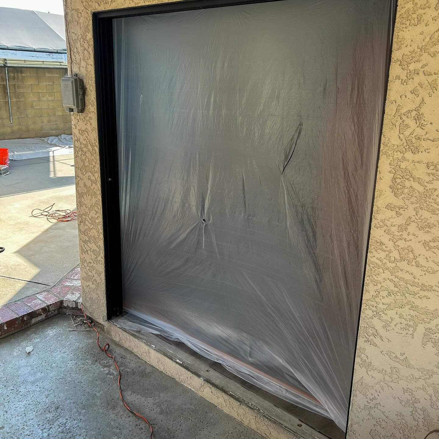 Covered doorway opening with black plastic sheeting in a stucco exterior wall
