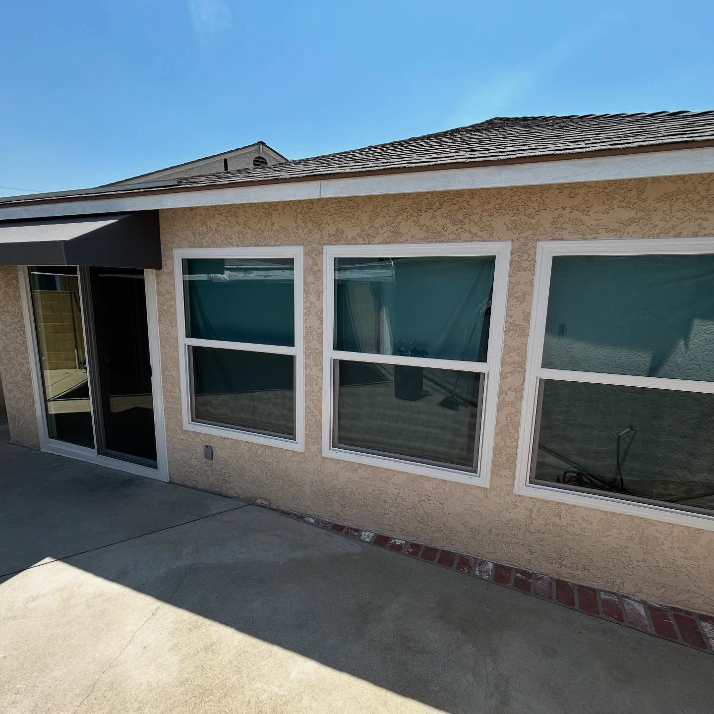 Stucco house exterior with three windows, a tiled roof, and a concrete patio.