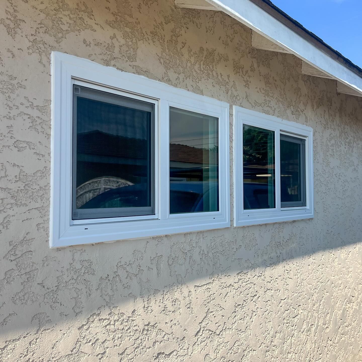 White-trimmed windows on a beige stucco house exterior under a blue sky