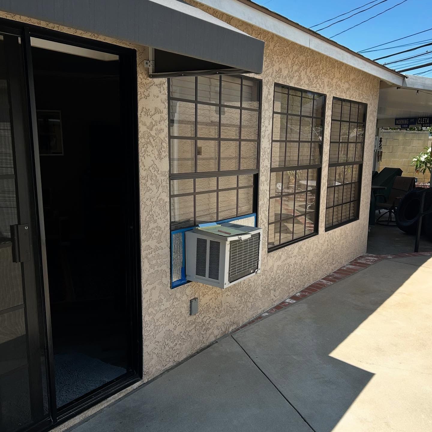 Exterior stucco wall with barred windows and a wall-mounted air conditioner beside a sliding door