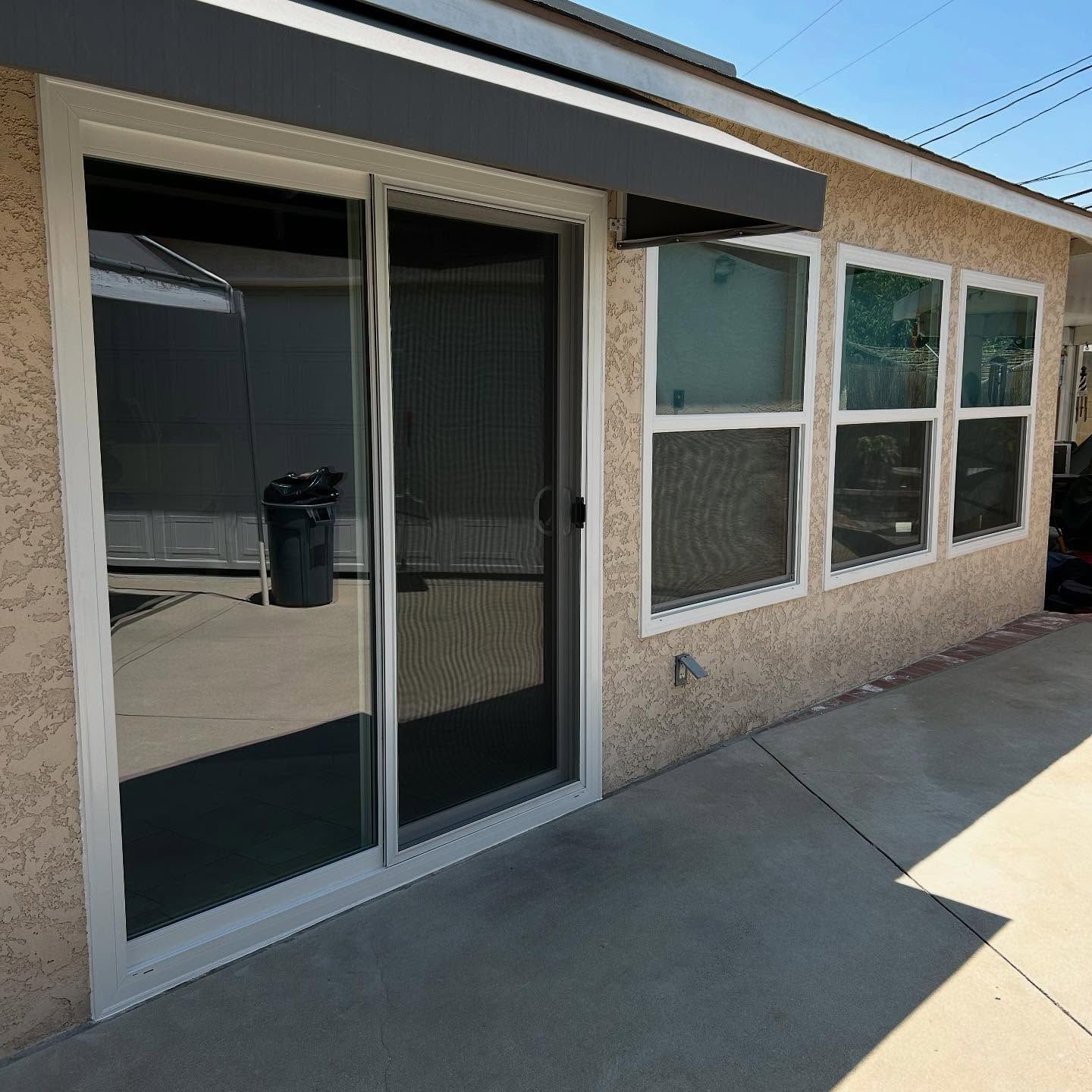 Patio sliding glass door and windows on a beige house exterior under a covered roof