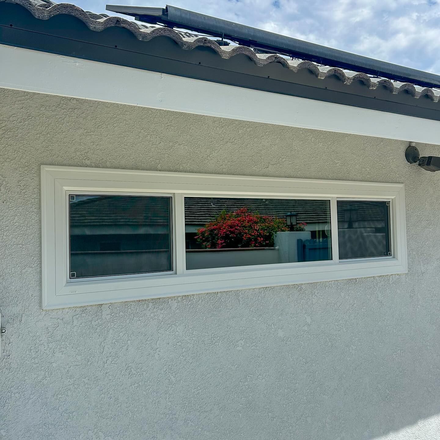 White stucco house wall with a narrow horizontal window and flower planter inside