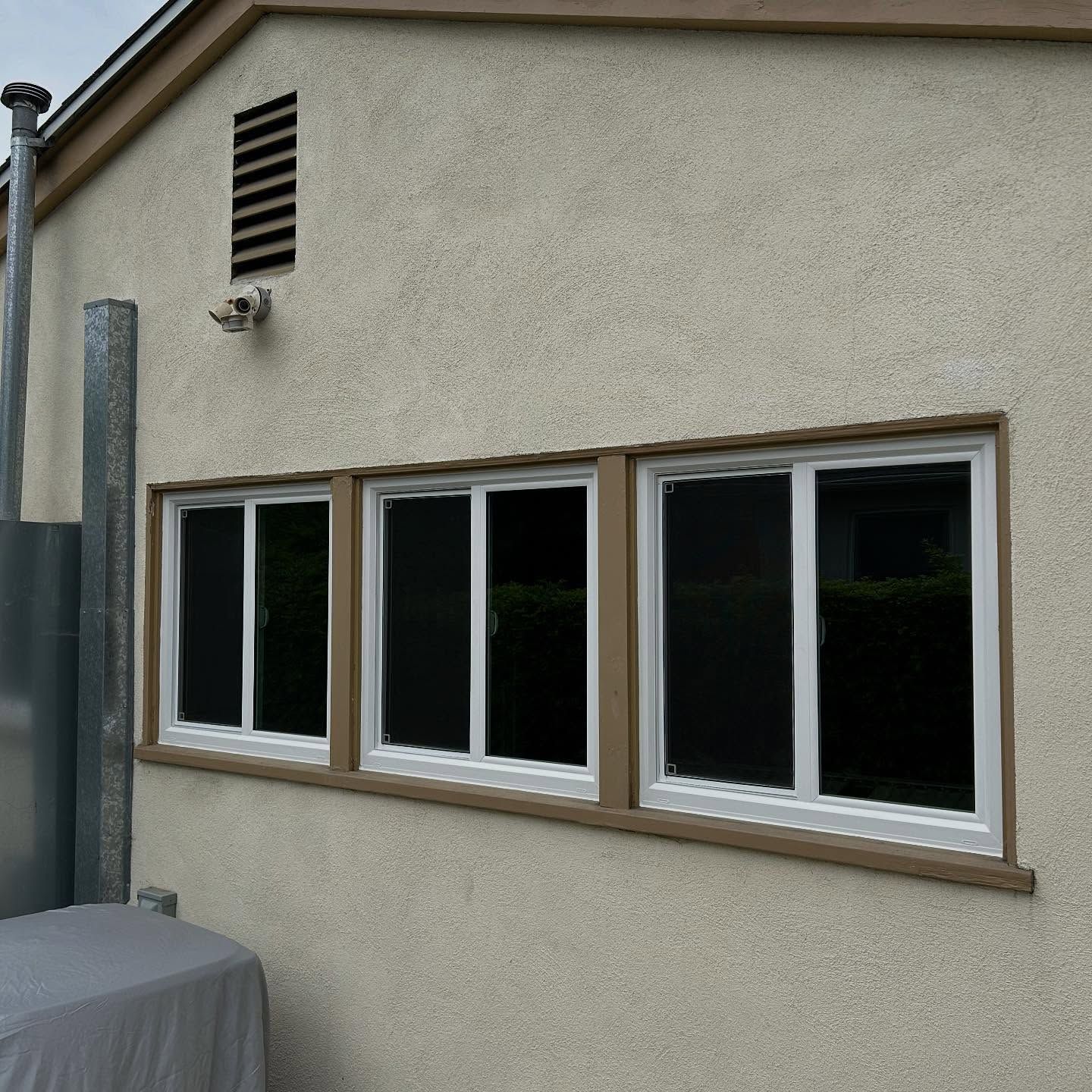 Exterior stucco wall with four windows, vent, and a downspout on the left side