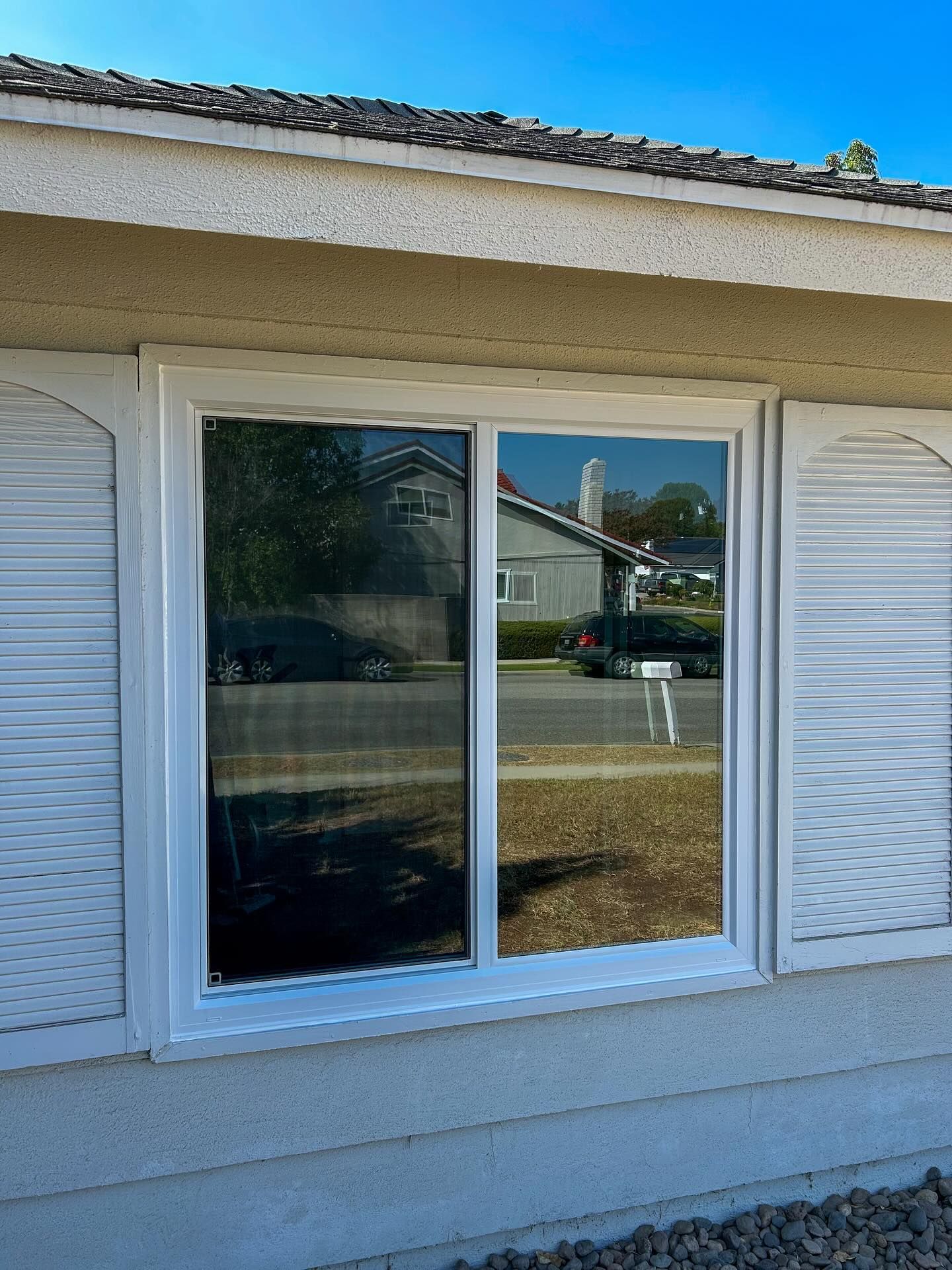 White-framed double sliding window on a beige stucco house exterior, reflecting a quiet neighborhood street.