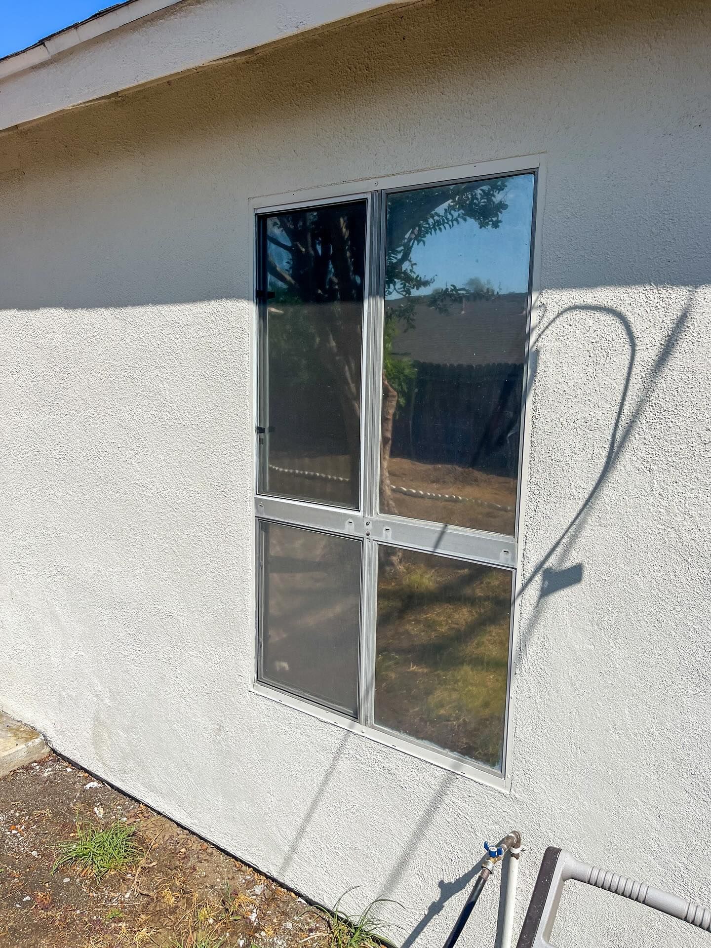 Exterior wall with a narrow window and dark metal bars, beside a coiled hose and outdoor faucet.