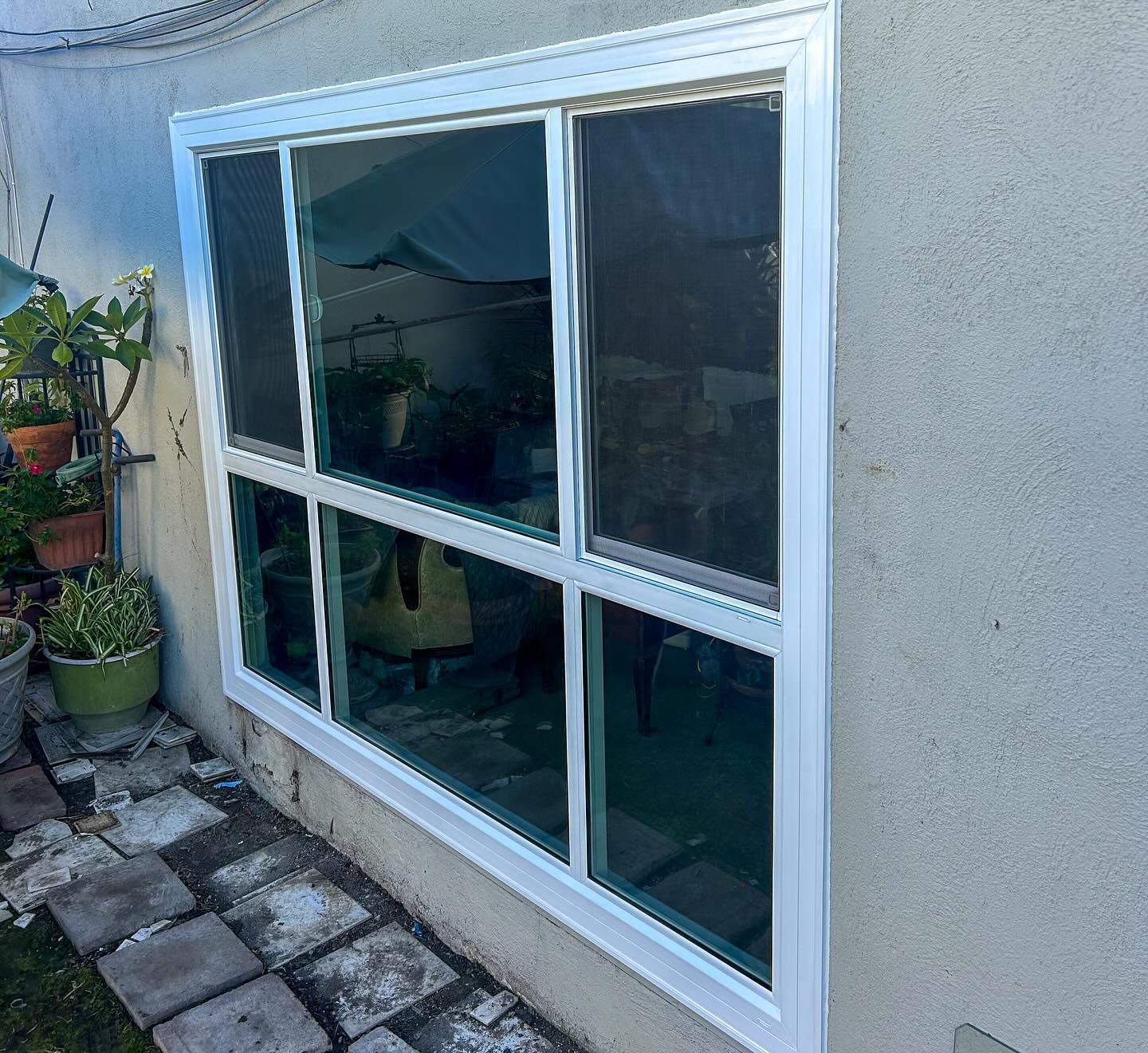 White-framed window on a stucco exterior wall beside a stone patio and potted plant.