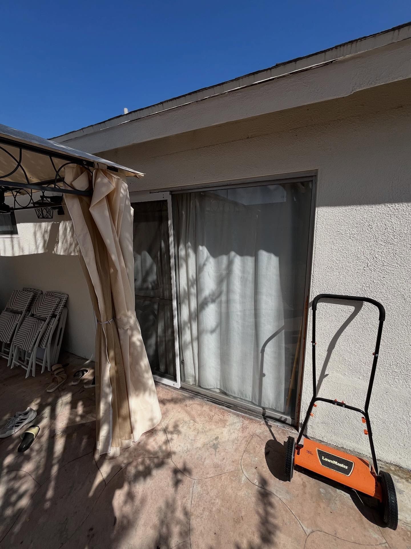 Patio with sliding glass door, tree shadow, and orange hand truck beside a stucco house