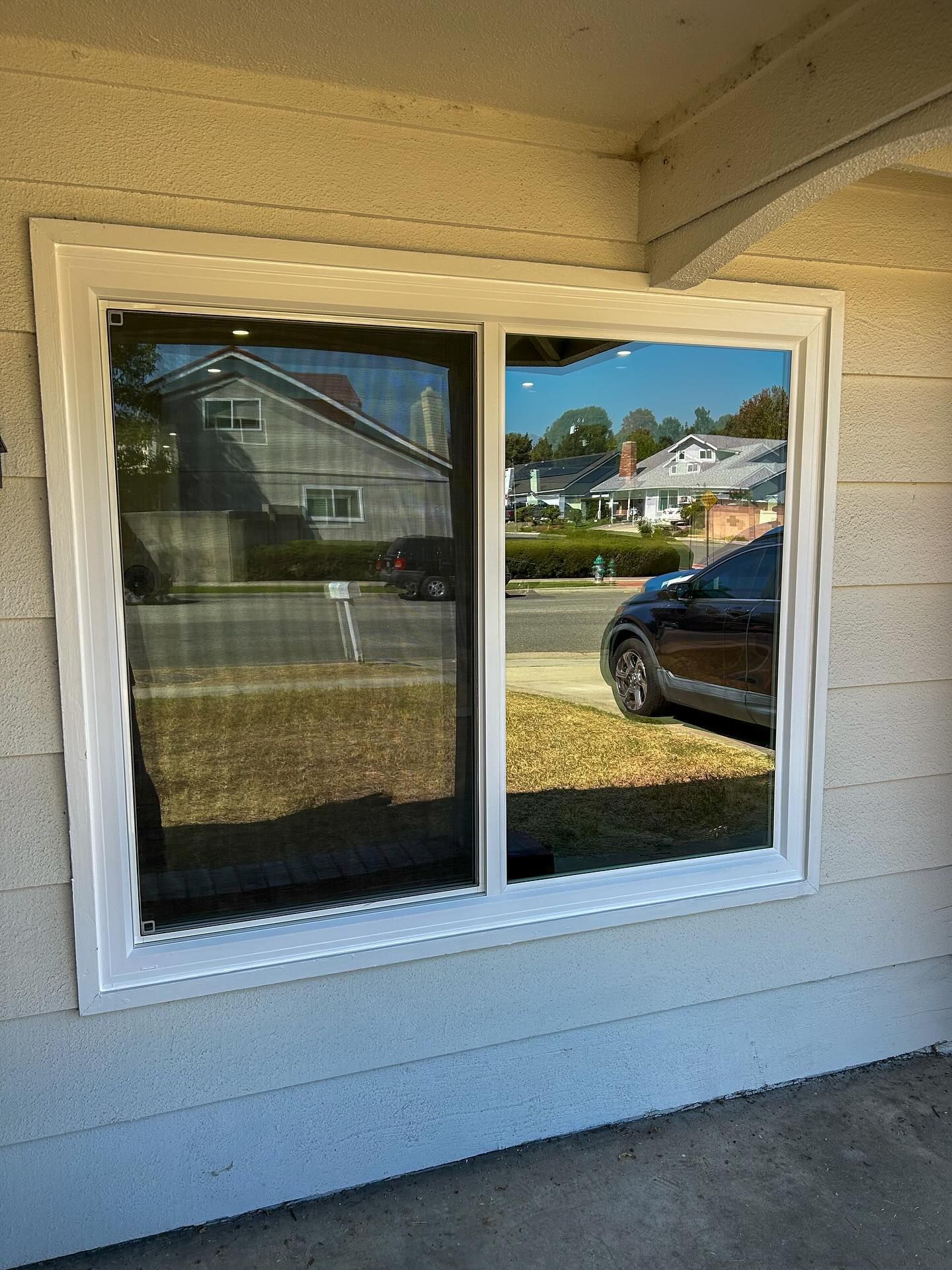 White-framed sliding window on a beige house exterior reflecting a suburban street and parked car