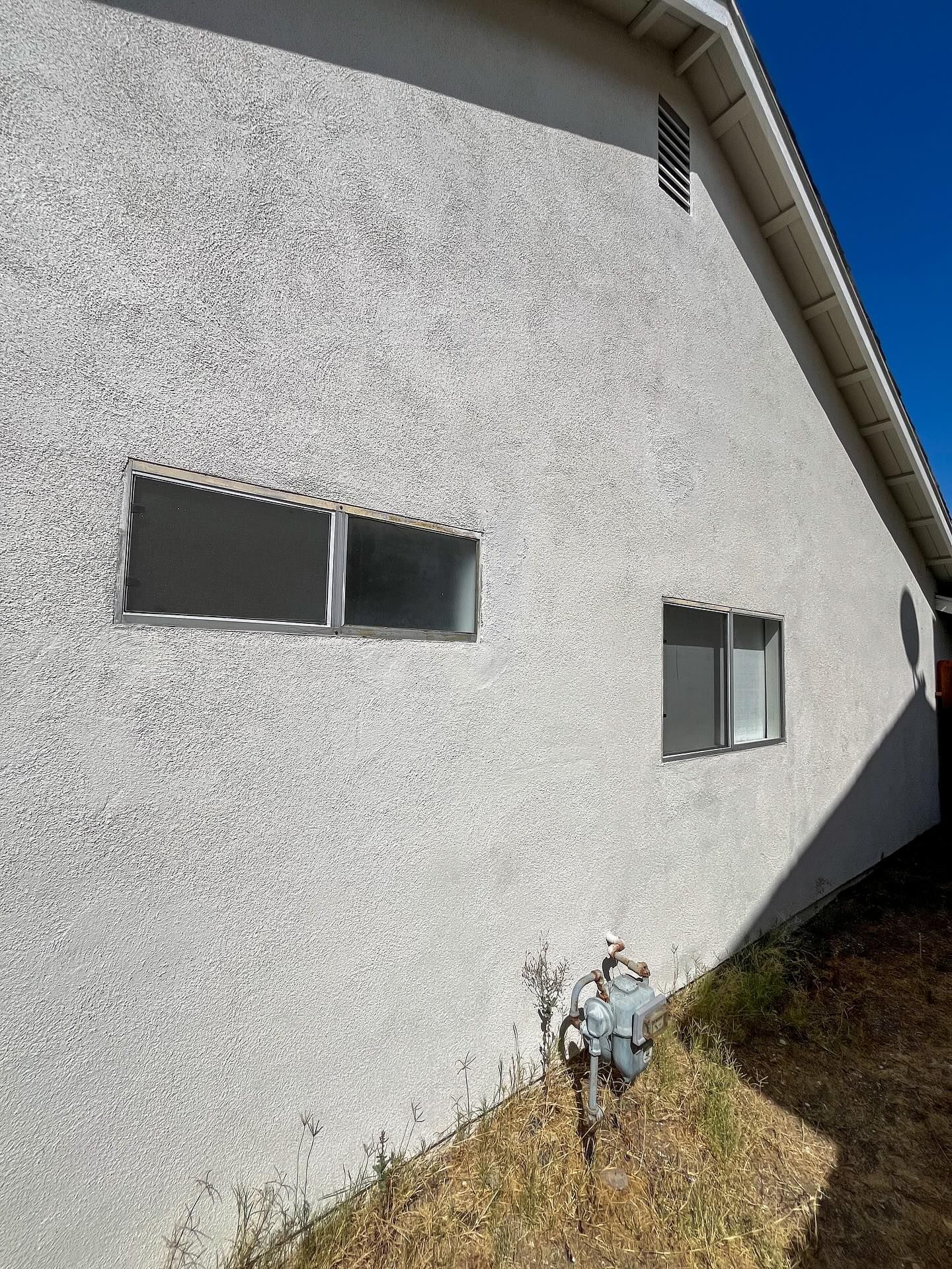 White stucco building side with two small windows and utility meters near the base.