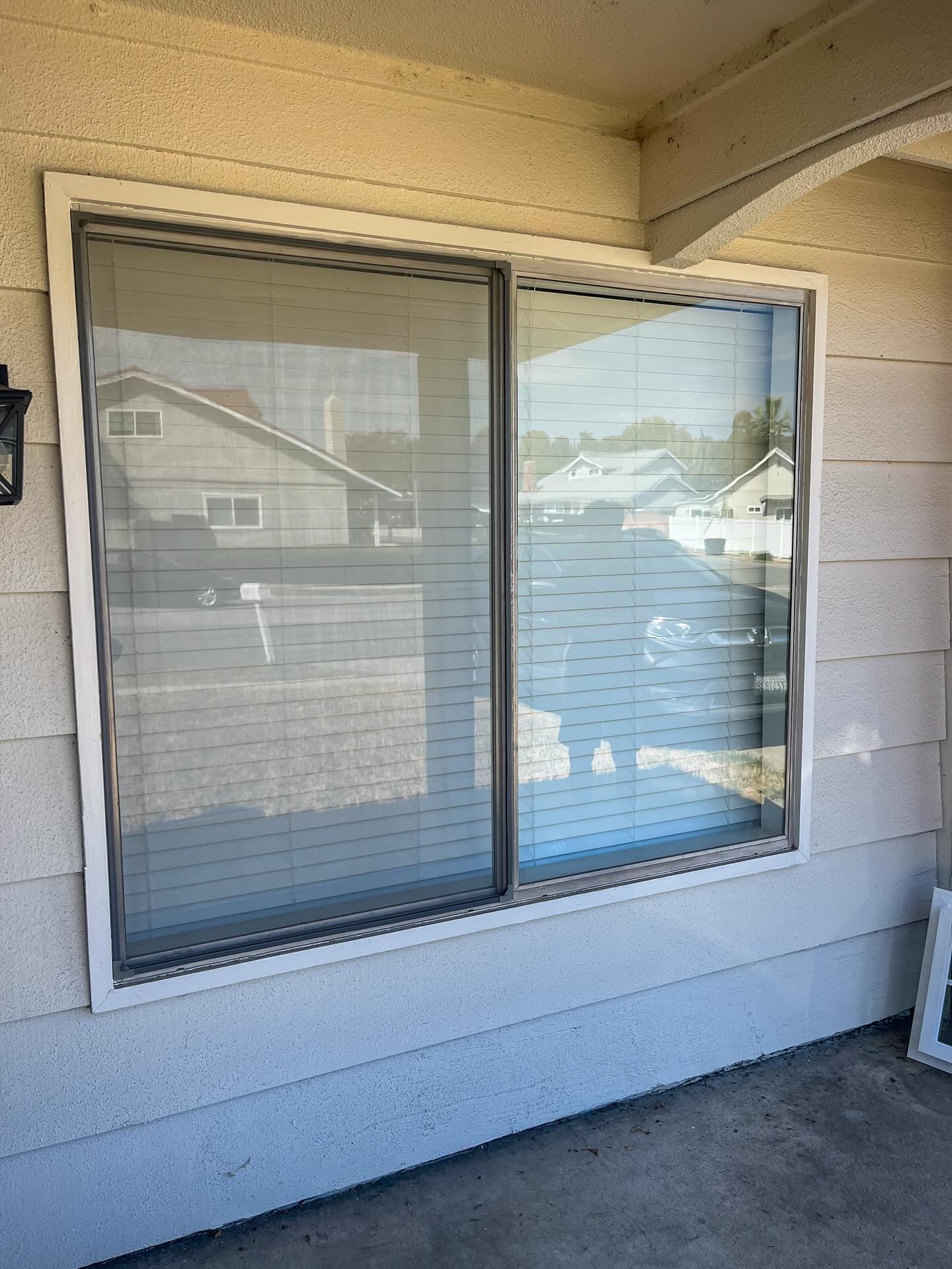 Sliding glass window with closed blinds on a beige exterior wall under a covered patio