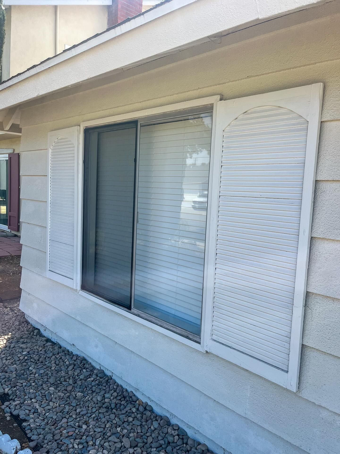 Exterior wall with a sliding glass door and white shutters beside it.