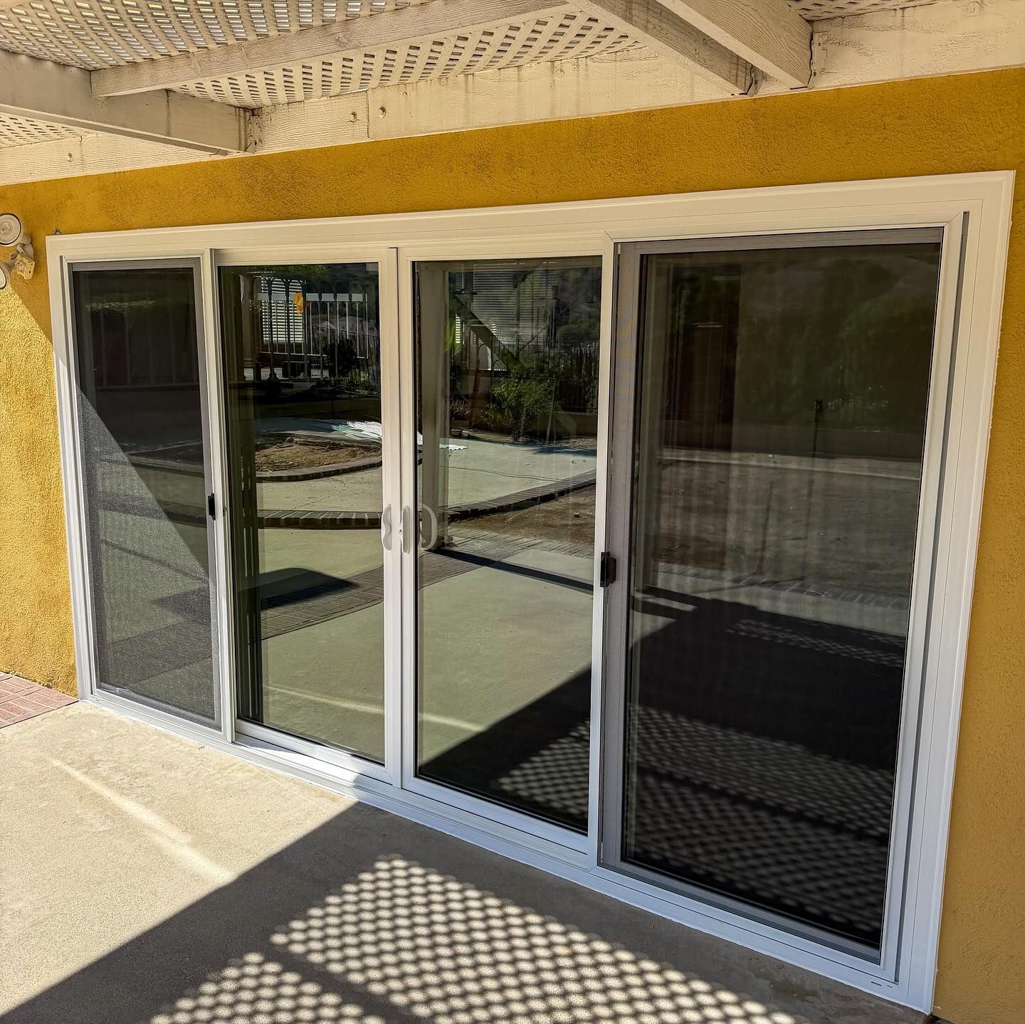 White-framed sliding glass doors and windows on a yellow stucco building with a sunlit patio.