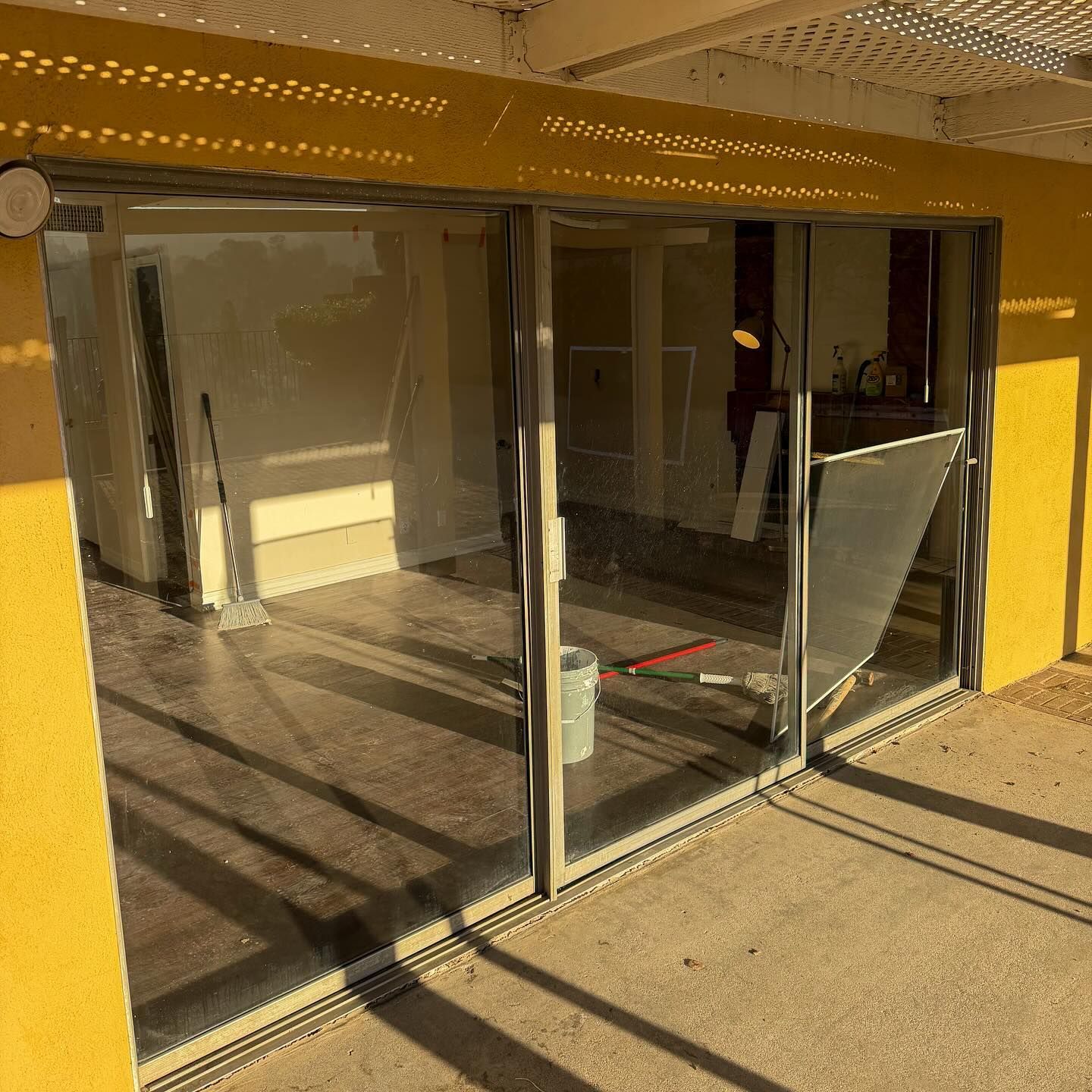 Broken glass sliding storefront door in a sunlit yellow building entryway