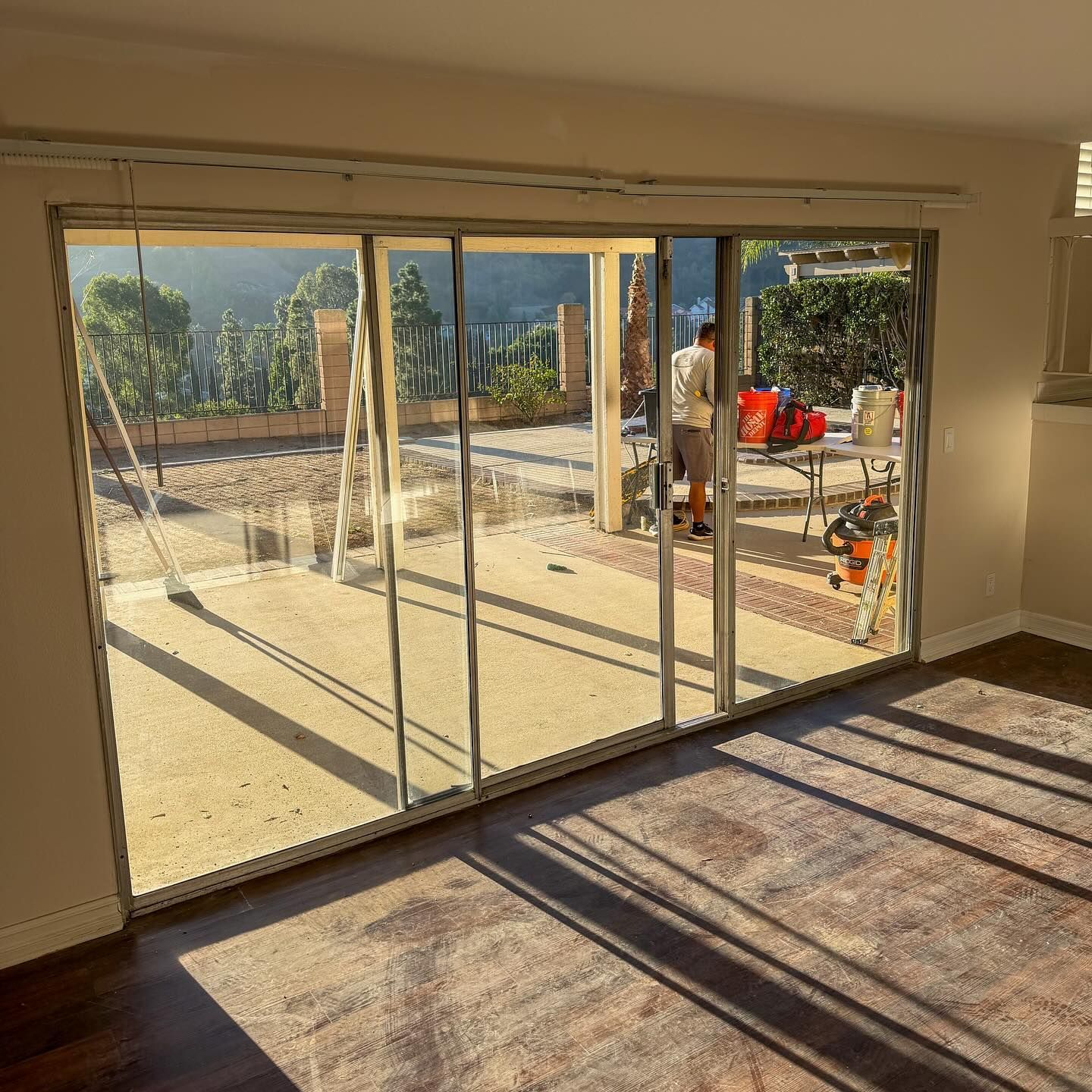 Sunlit living room with sliding glass doors opening to a patio and garden, long shadows across the floor