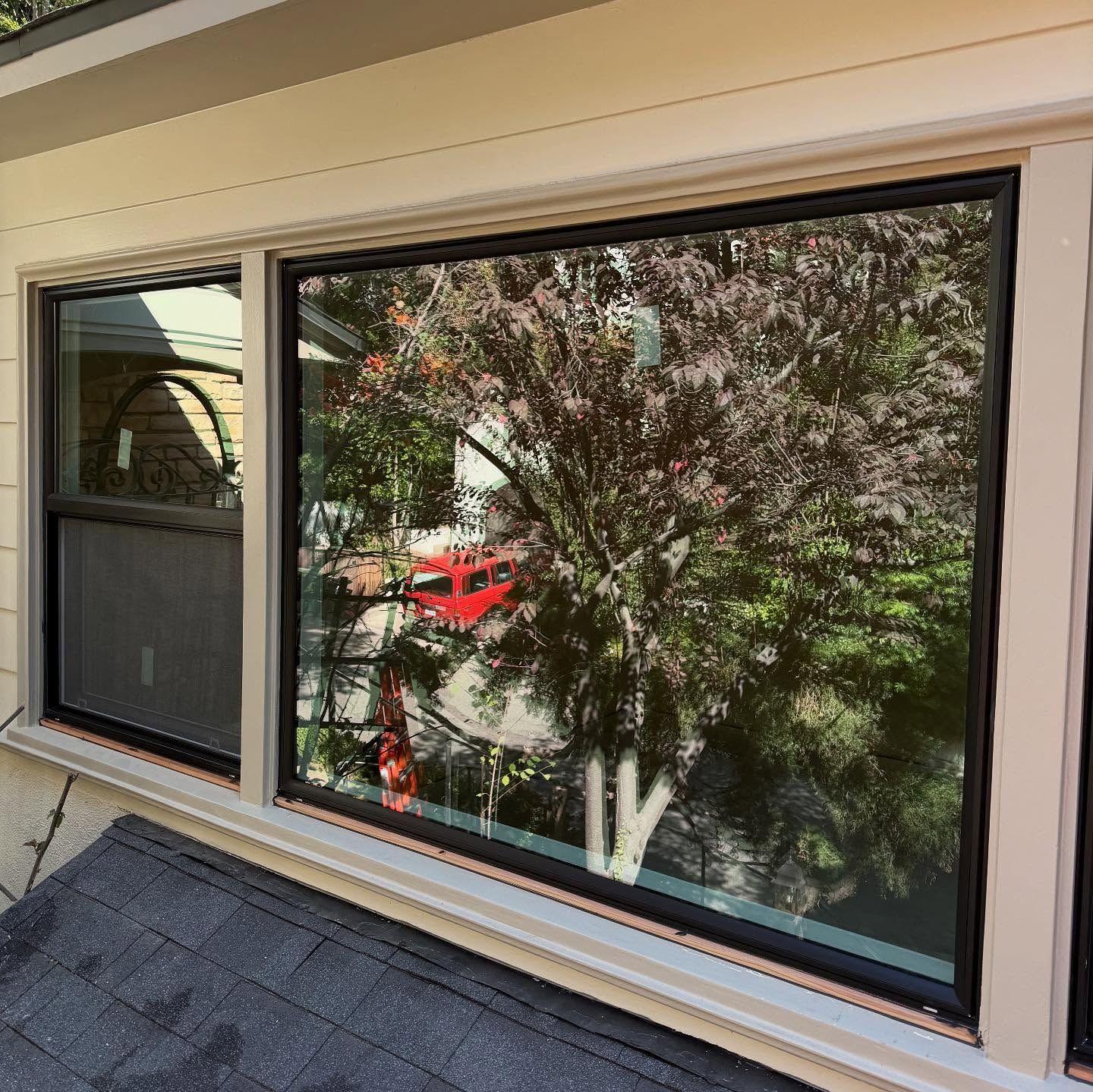 Sliding glass window reflecting trees and a red car, with a screened door beside it.