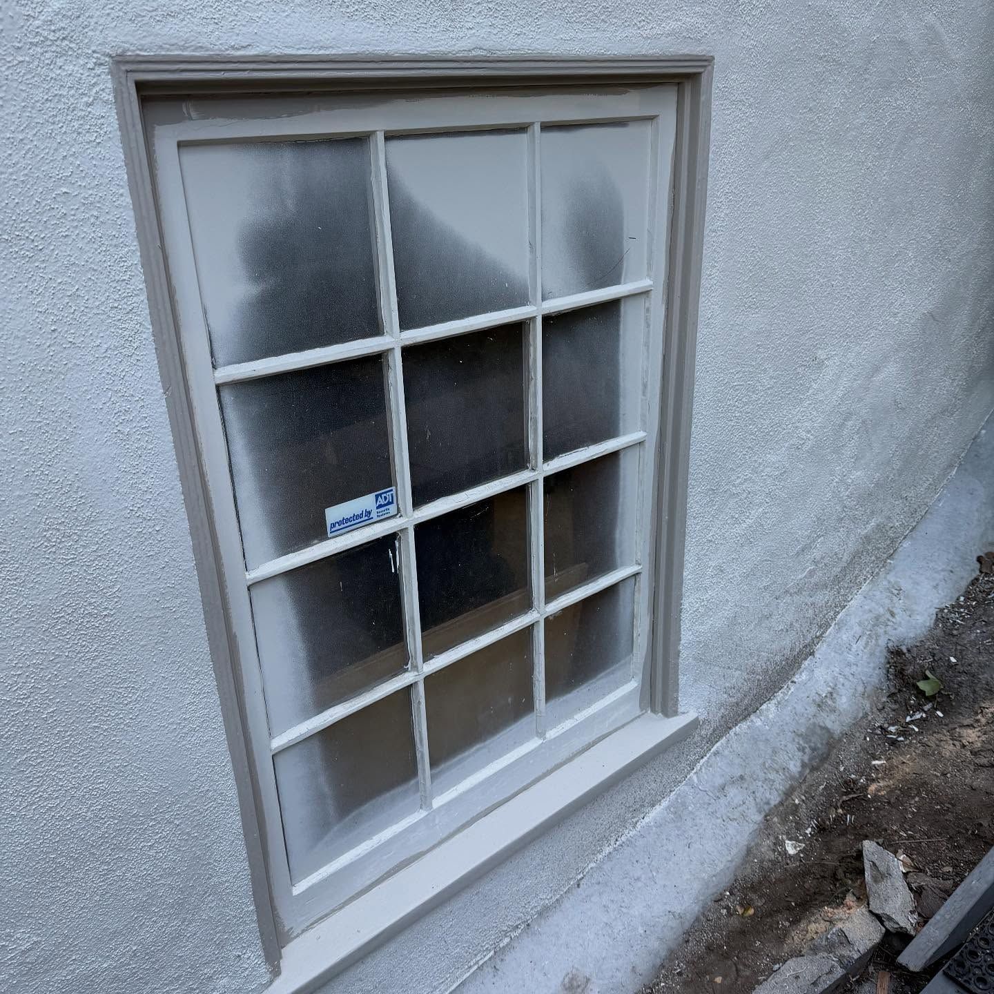 Small basement window with frosted glass panes set in a stucco wall.