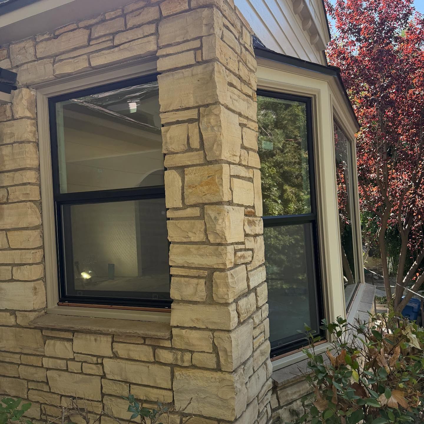Stone house corner with bay windows and a red-leaf tree beside it