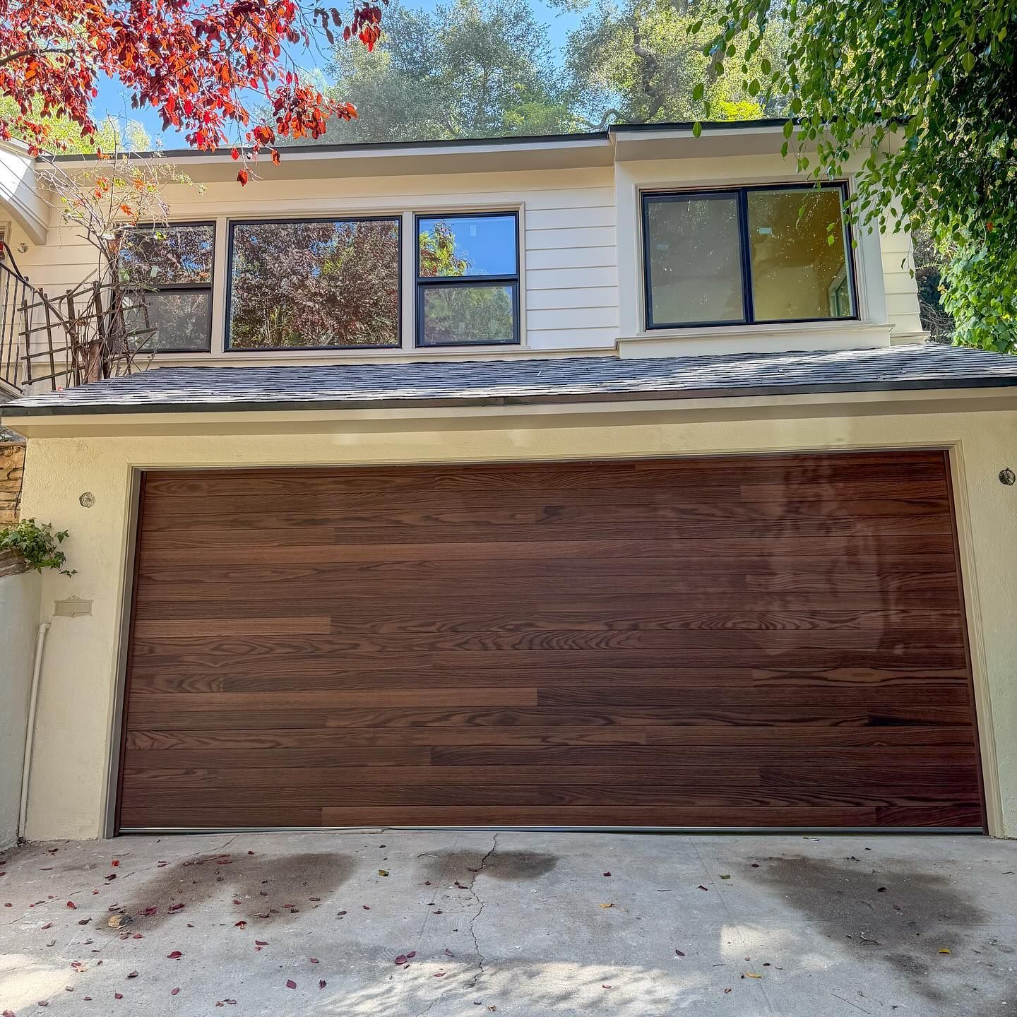 Two-story house with a wide wooden garage door and white exterior, seen from the driveway.