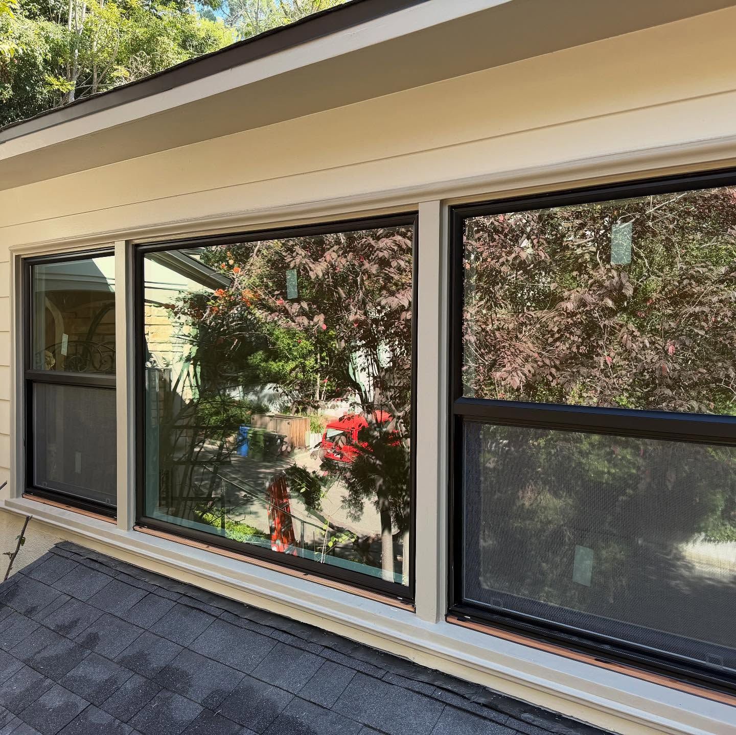 Three large windows in a beige exterior wall above a shingled roof with garden reflections