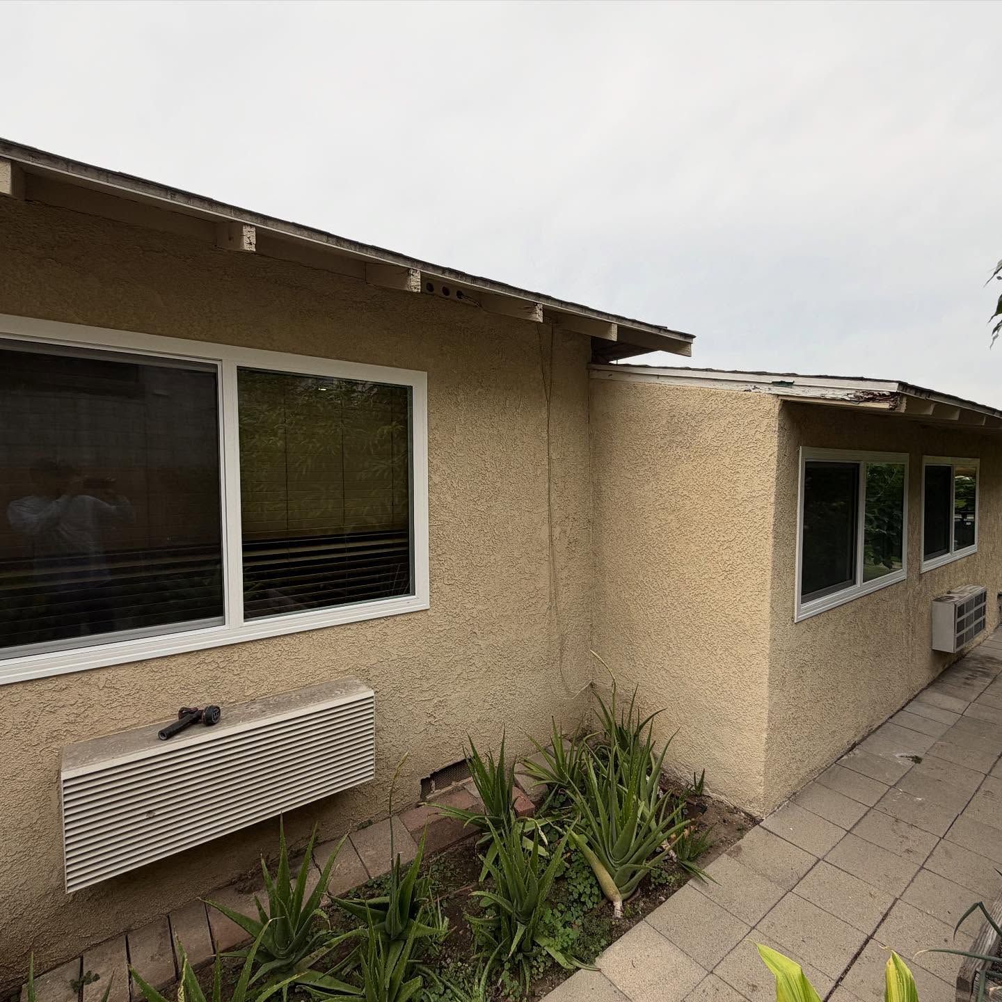 Exterior of a beige stucco house with large windows, potted plants, and a tiled walkway