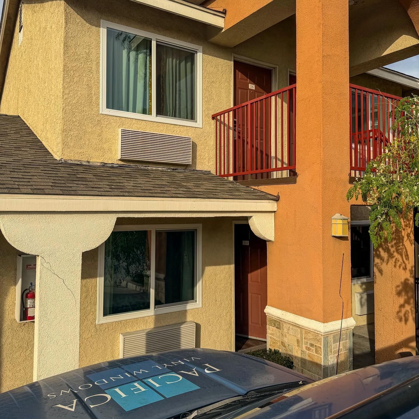 Two-story beige house with red balcony railing and a parked car in front