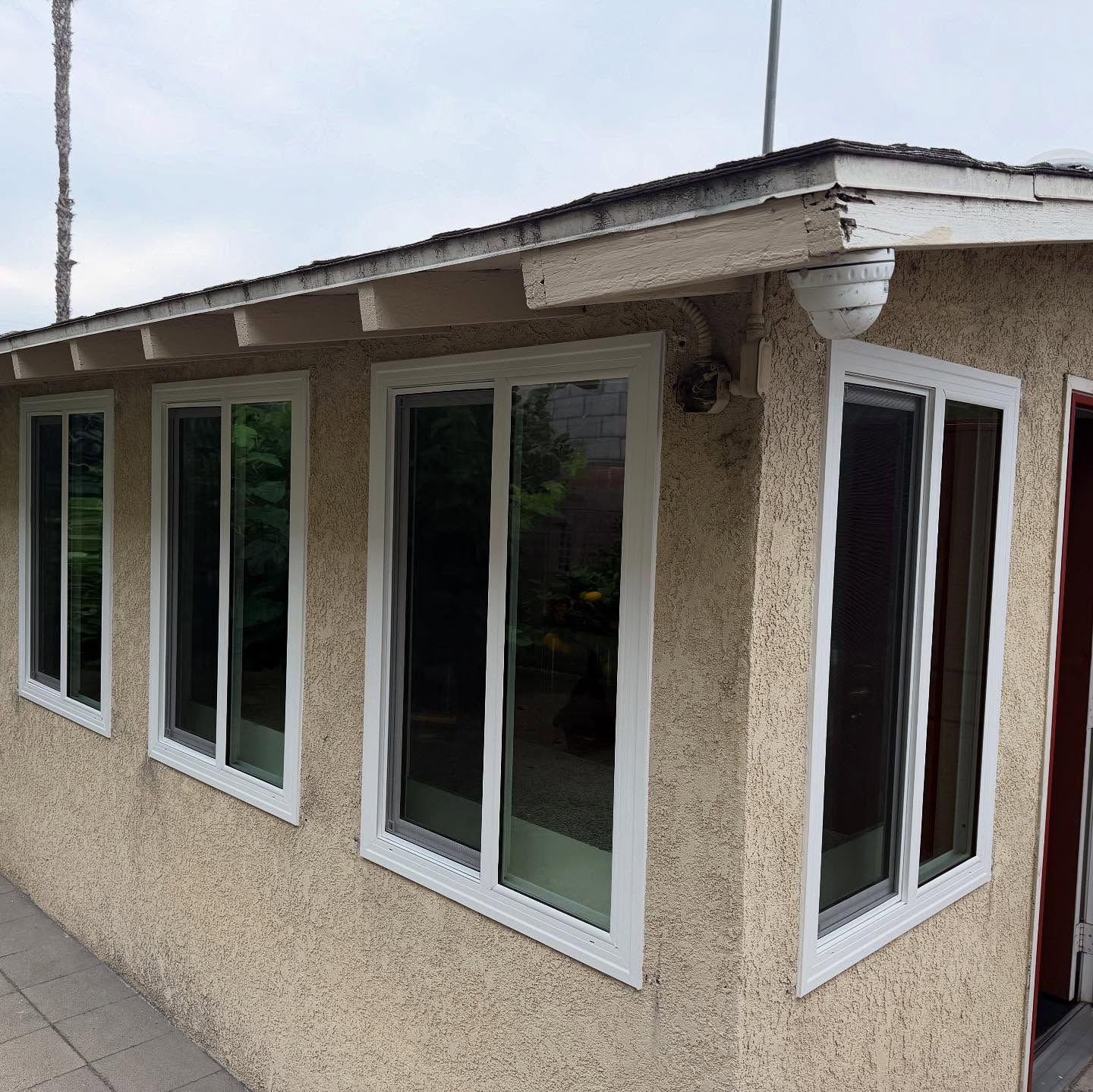 Corner view of a beige stucco house with white-framed windows and a small overhang roof
