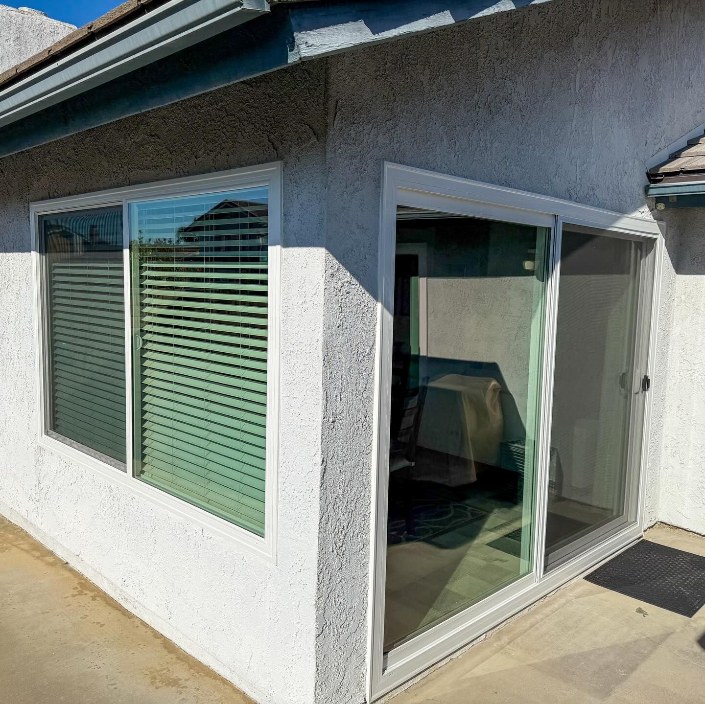 Exterior of a stucco house with large windows and a sliding glass door on a sunlit patio