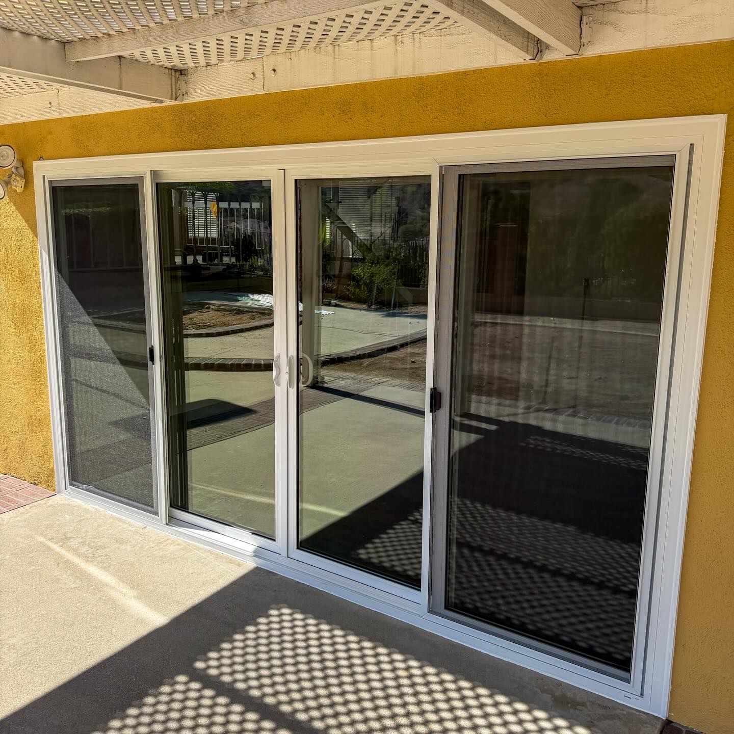 Four-panel white sliding glass door with security mesh on a yellow building patio