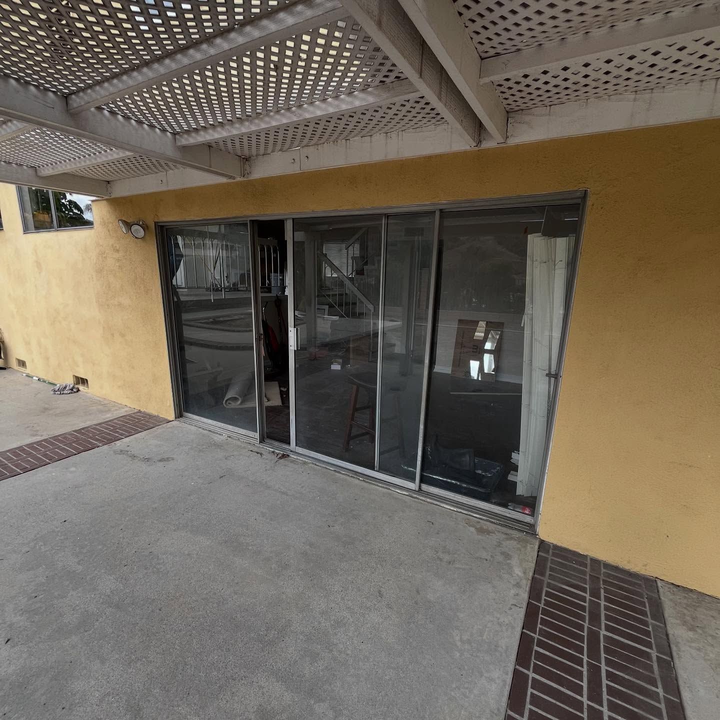 Covered patio with yellow walls and sliding glass doors, viewed from a concrete walkway.
