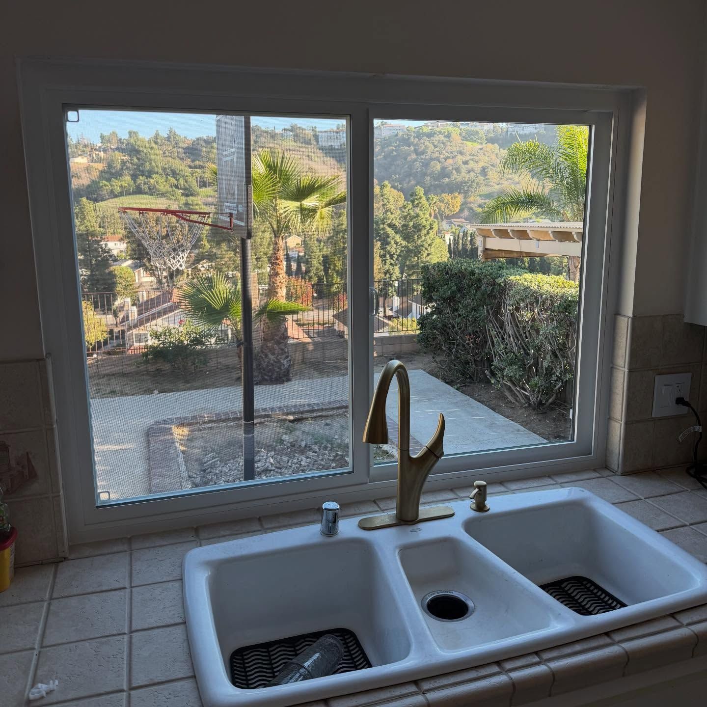 Kitchen sink under a window overlooking a sunny backyard and hills