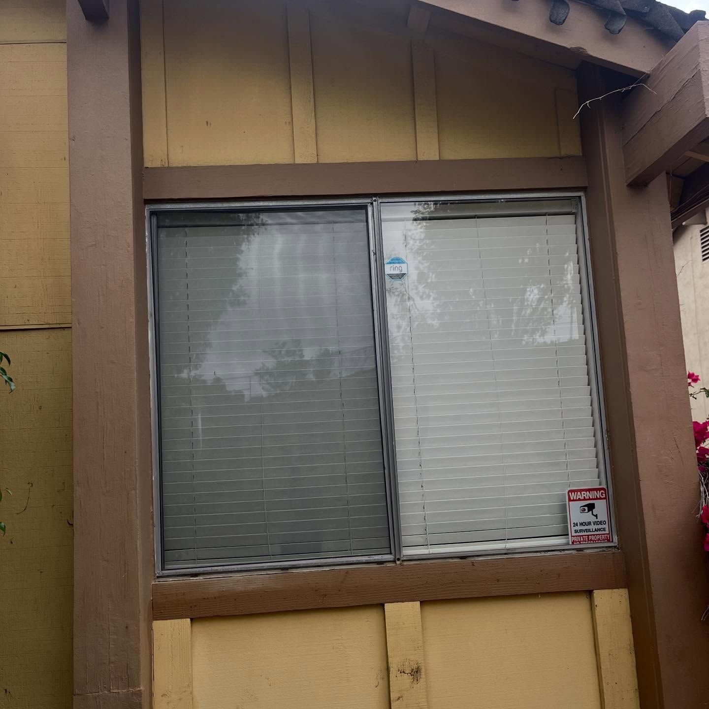 Small tan house exterior with a sliding window and a closed blind behind glass
